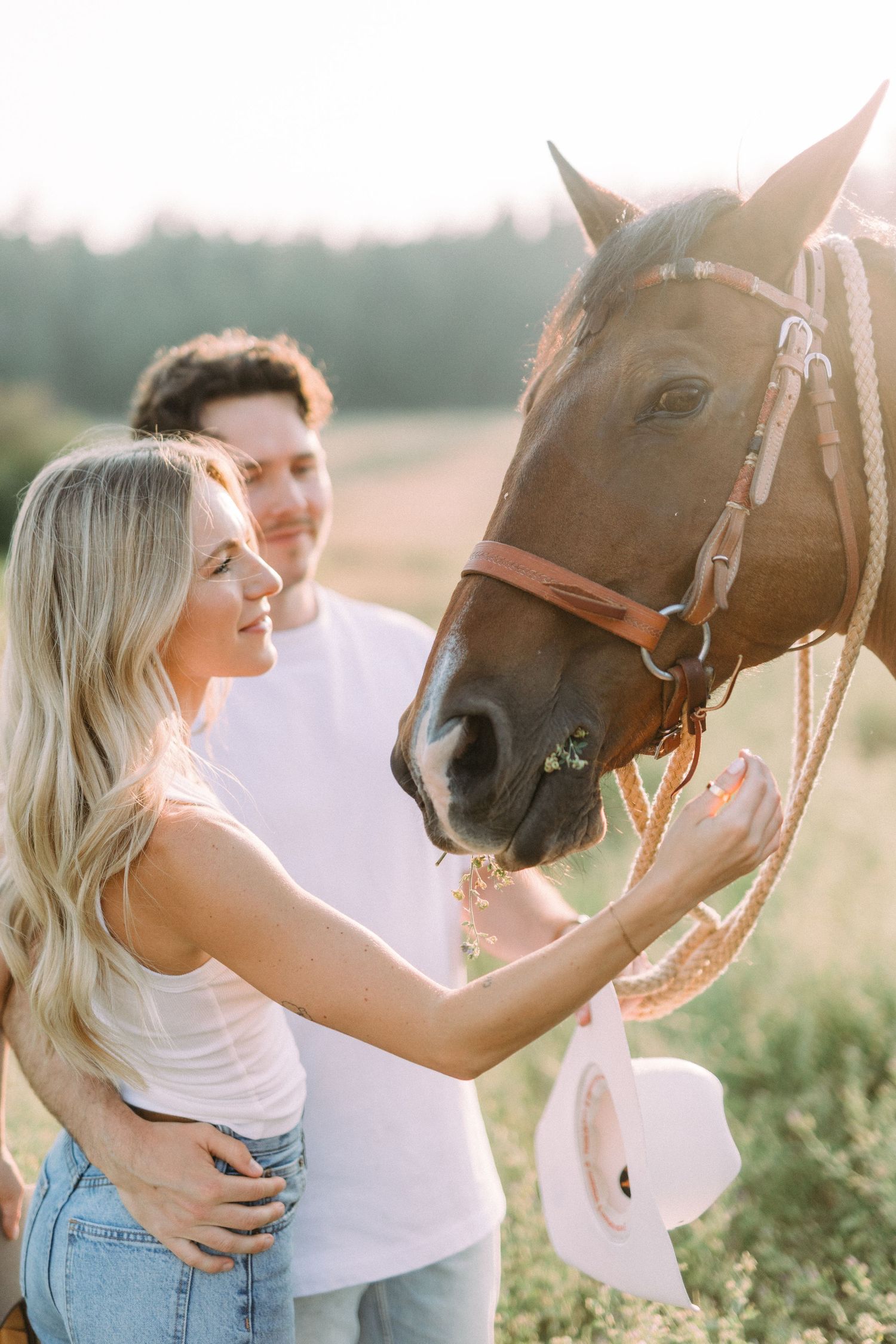Couple bonding with their horse in a sunlit field during golden hour.