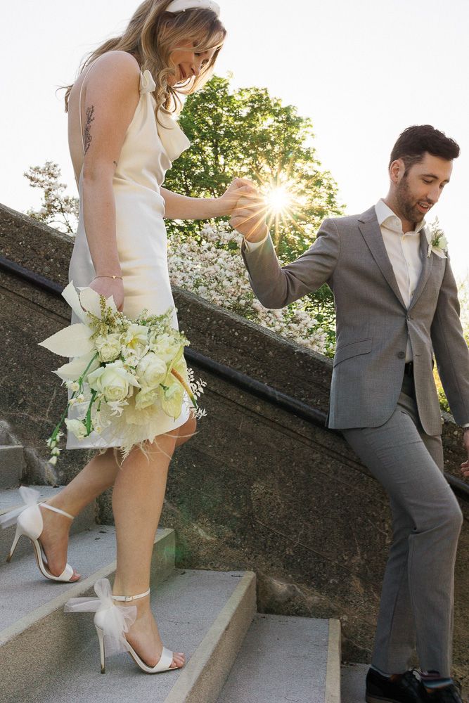 A couple ascending stone steps at sunset, with the bride holding a white bouquet.