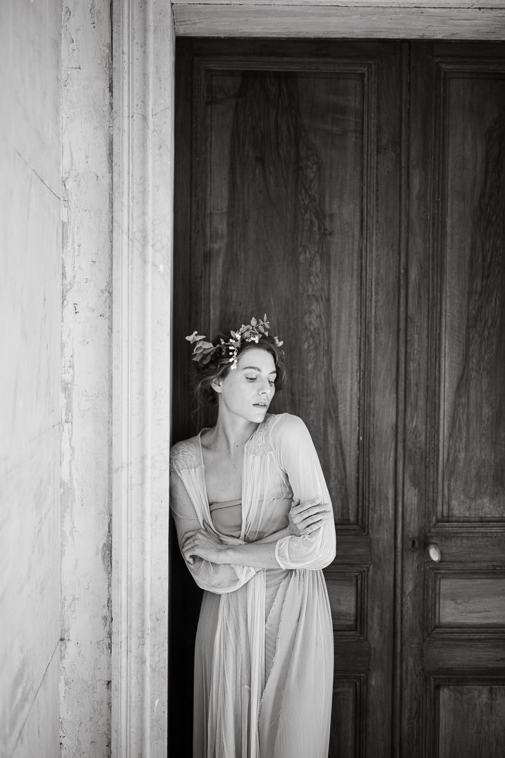 Dramatic black and white portrait showing ethereal pose against vintage wooden doors.