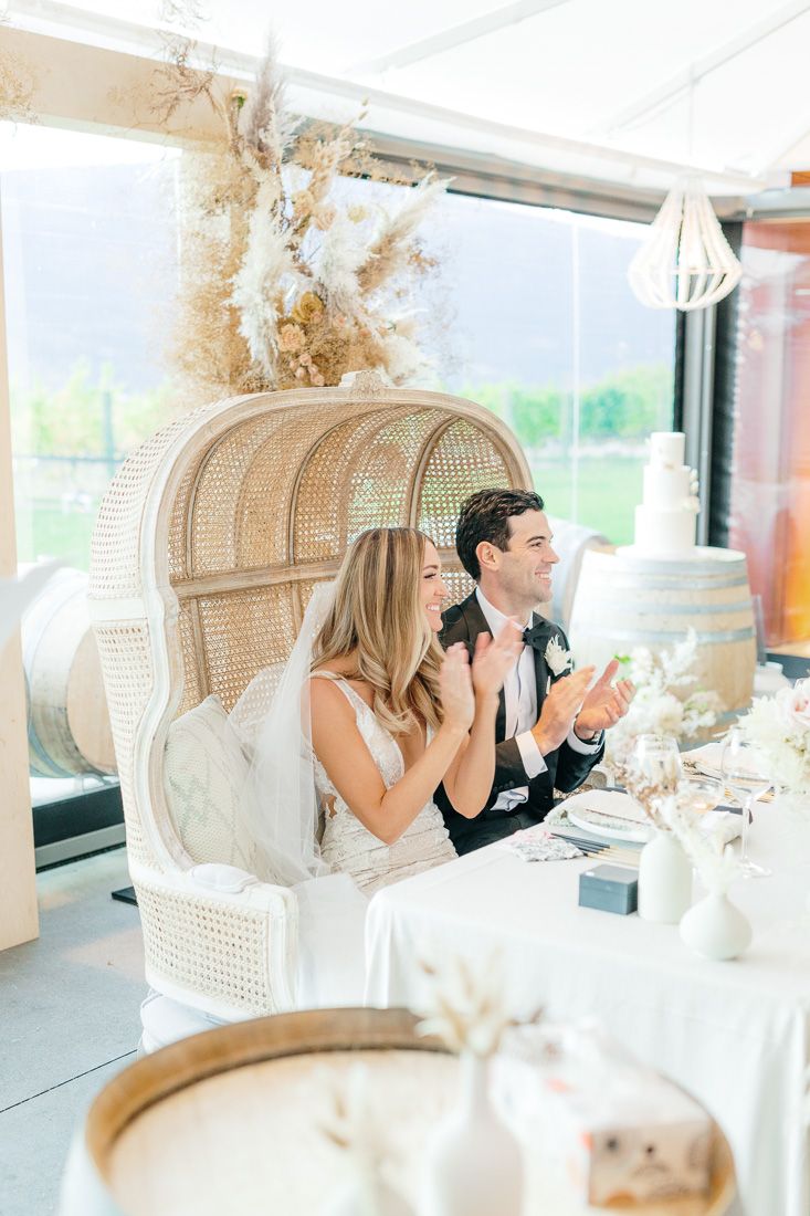 A couple seated in a peacock chair at their wedding reception with dried floral decorations.