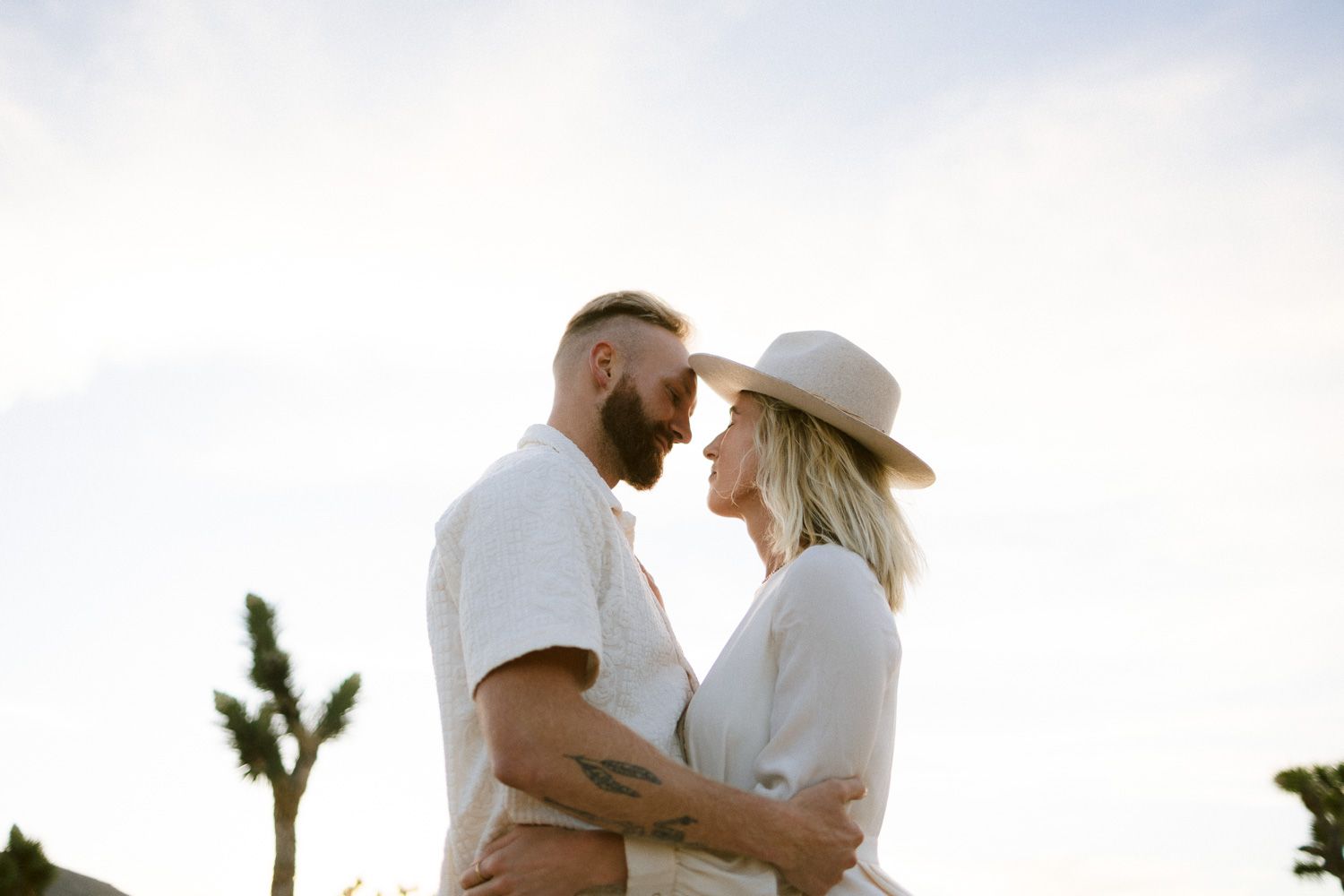 Sunset engagement photo with Joshua trees silhouetted against desert sky.