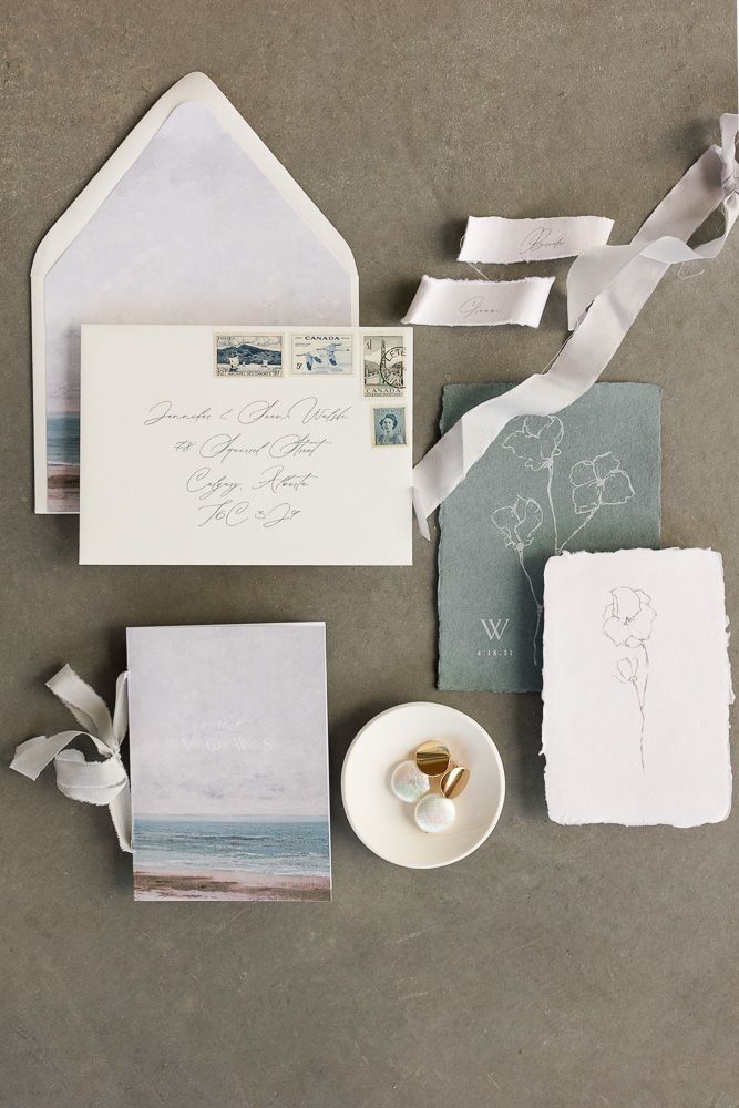 Wedding stationery collection featuring coastal artwork, white envelopes, and sage green accents.