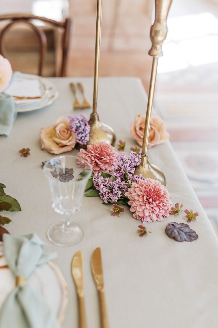 Close-up of wedding table decor with pink and lilac flowers, gold candlesticks, and elegant place settings.