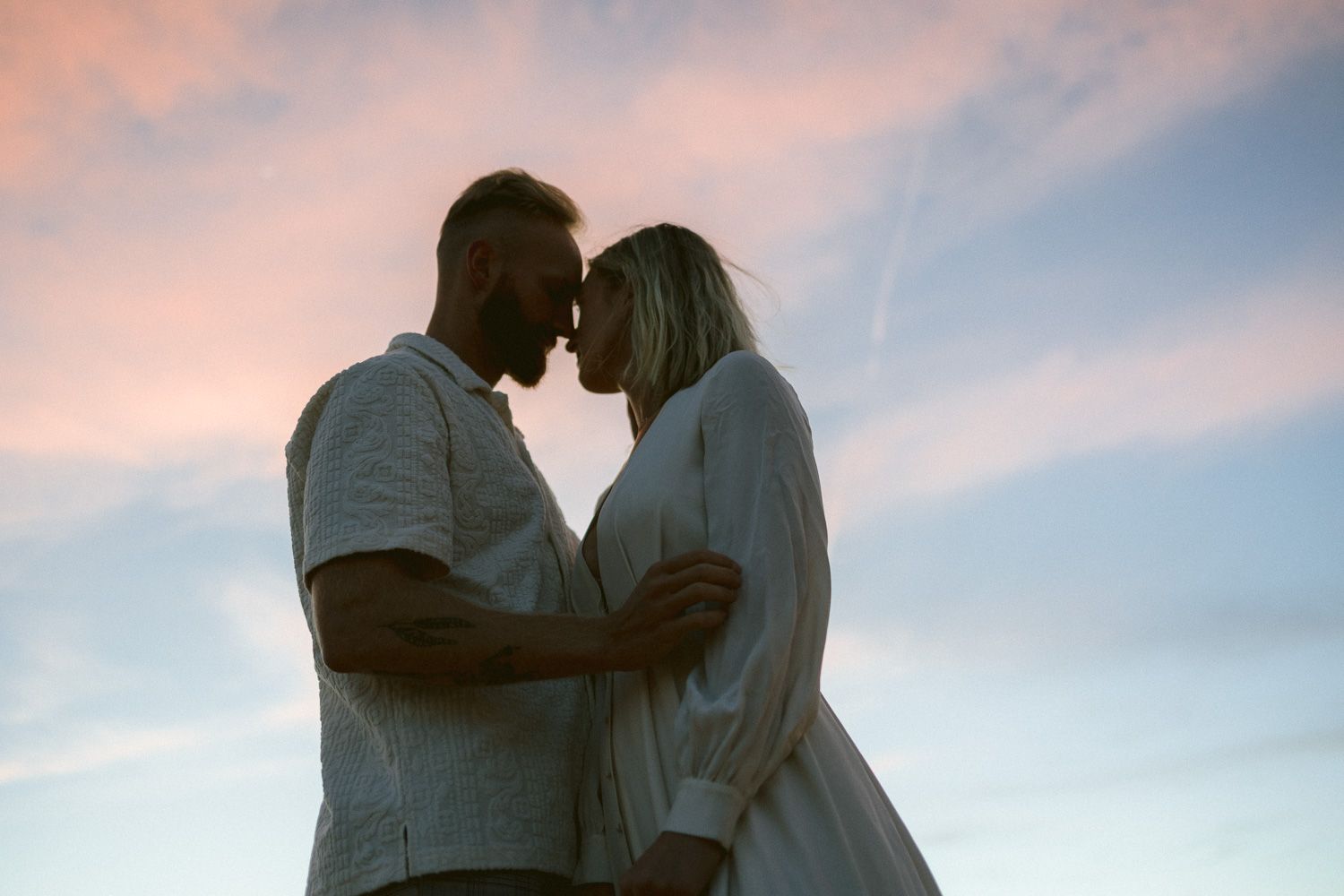 A silhouetted couple embraces against a pink and blue sunset sky.