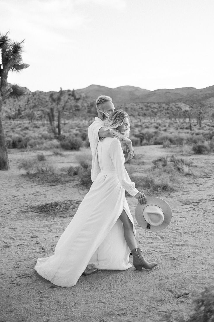 A black and white desert wedding photo capturing an intimate moment between a couple.