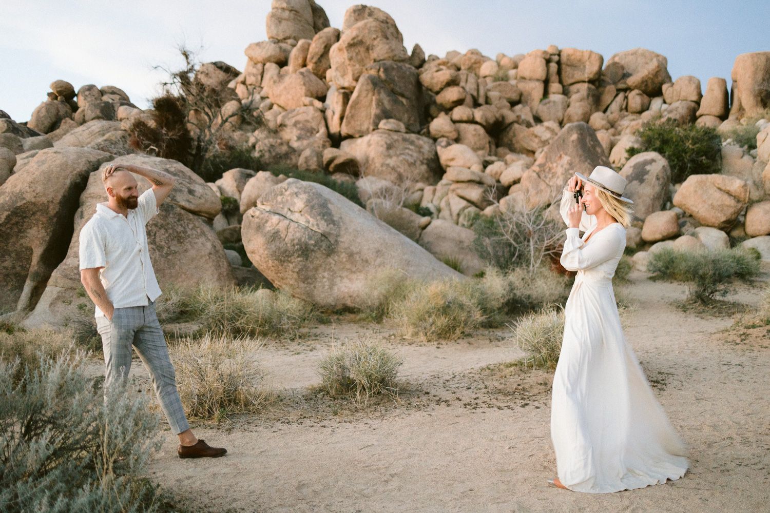 Two people stand on a desert trail surrounded by large boulders during a photo session.