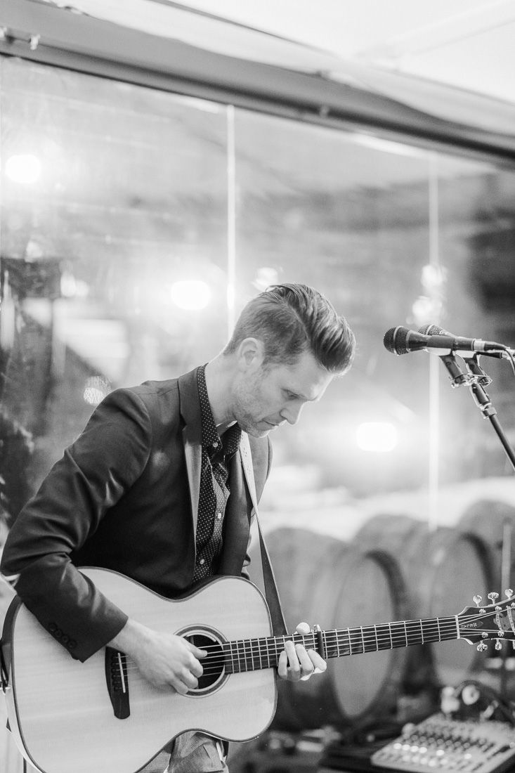 Wedding musician plays acoustic guitar and sings into microphone during reception performance.