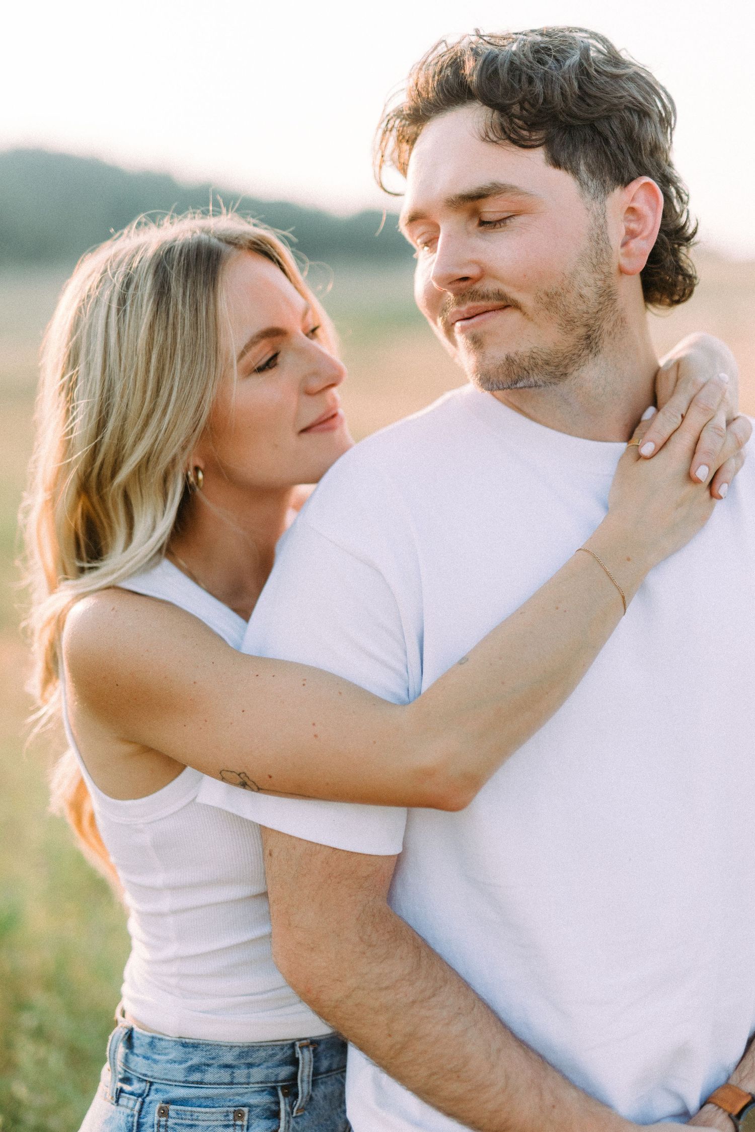 Couple embracing in casual white t-shirts against golden outdoor backdrop.