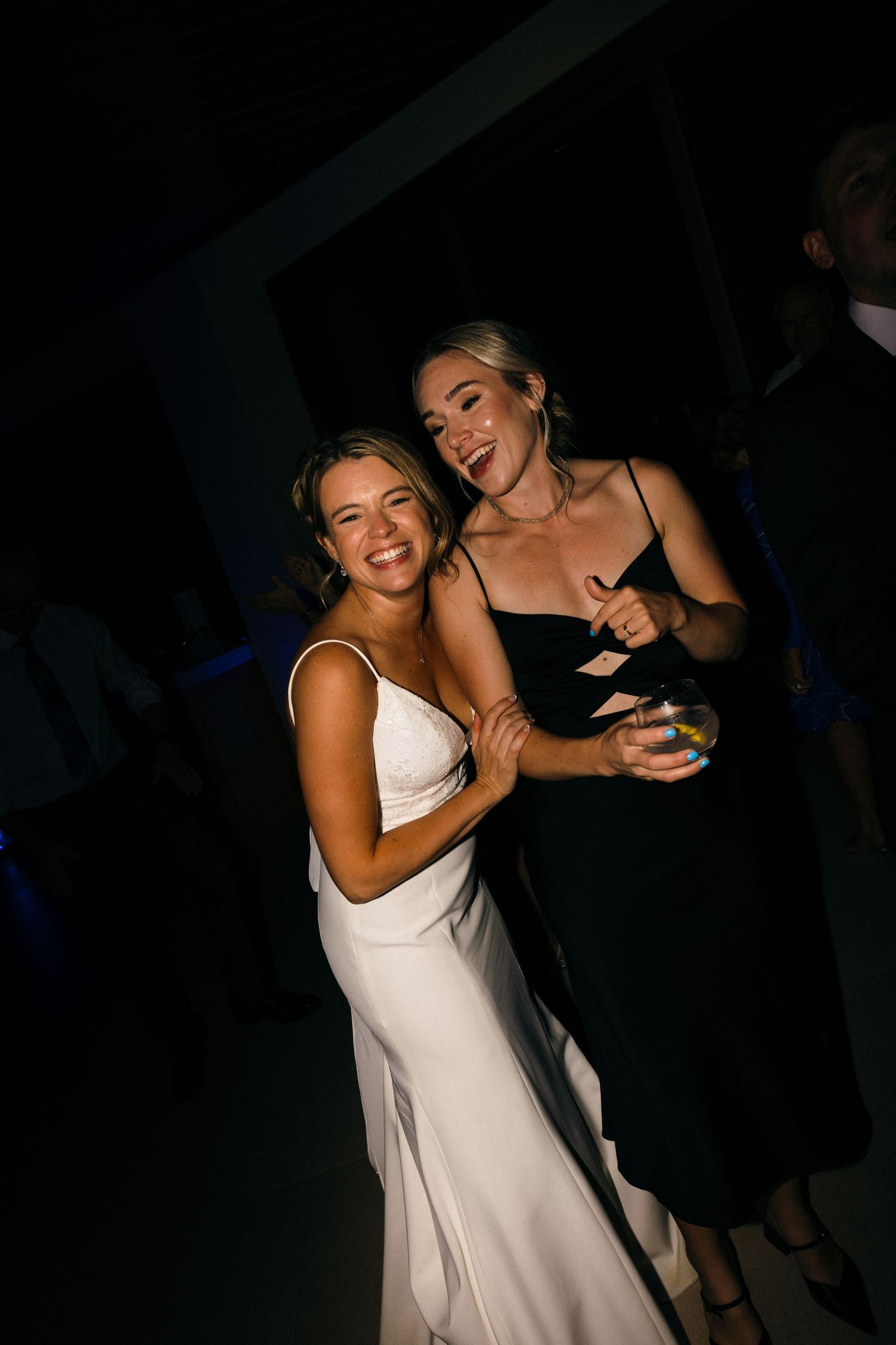 Wedding reception guests dancing and celebrating in a dark venue with dramatic lighting.
