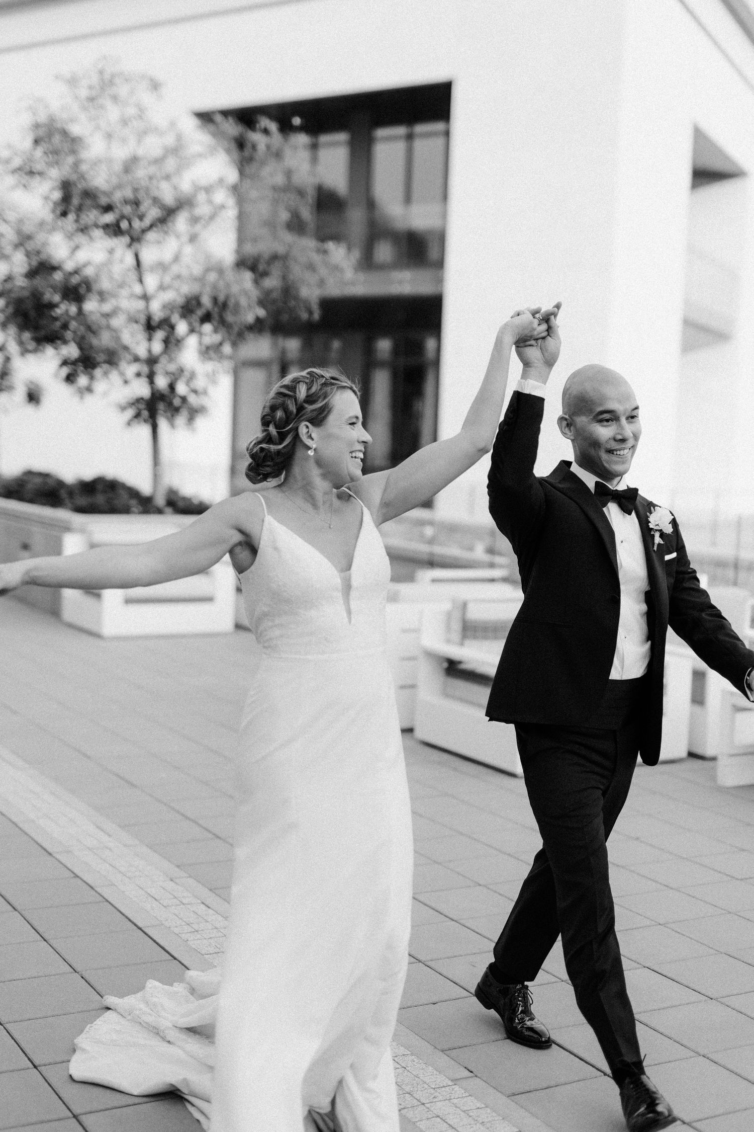 Newlyweds dancing joyfully on outdoor terrace in black and white photography.