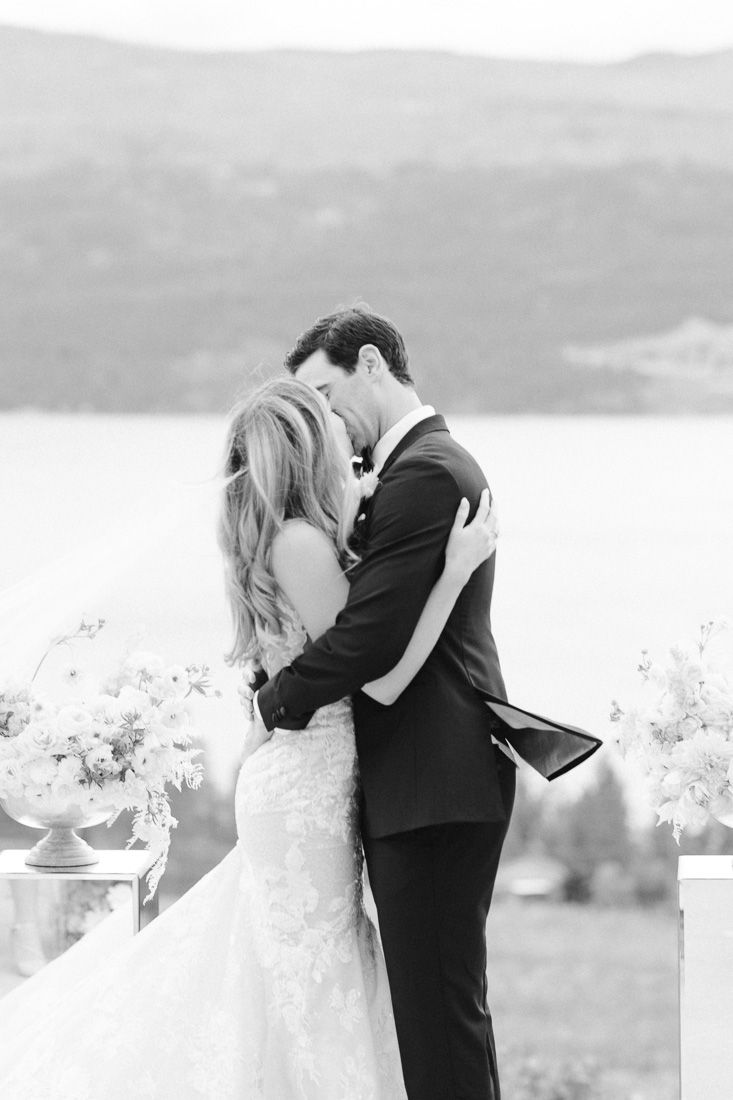 A romantic black and white wedding photo of a couple embracing against a mountain backdrop.