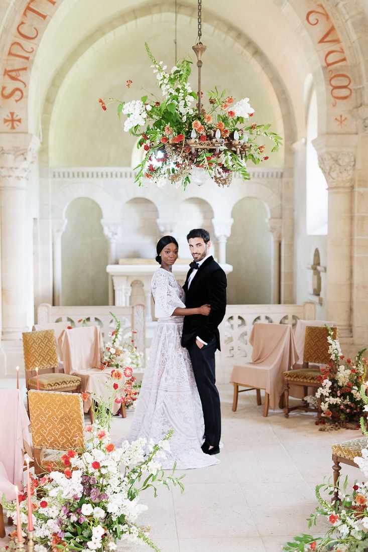 Elegant wedding ceremony setup in a classical arched room with floral arrangements and vintage chairs.
