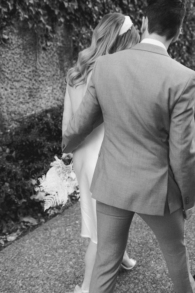 Black and white photo of a couple in formal wear standing close together outdoors.