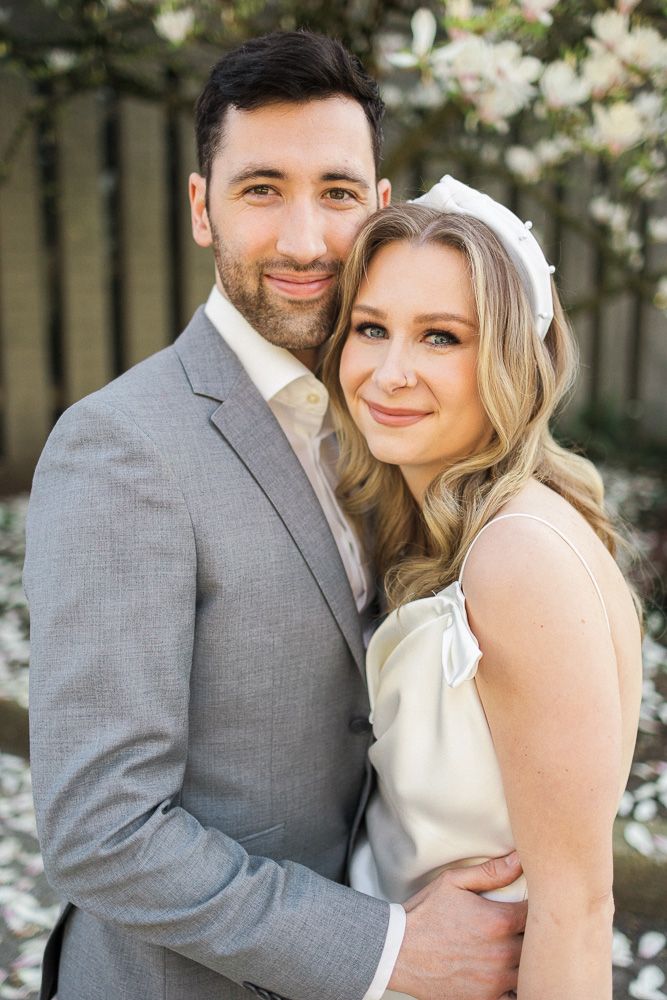 A romantic wedding portrait of a couple in formal attire embracing against a garden backdrop.