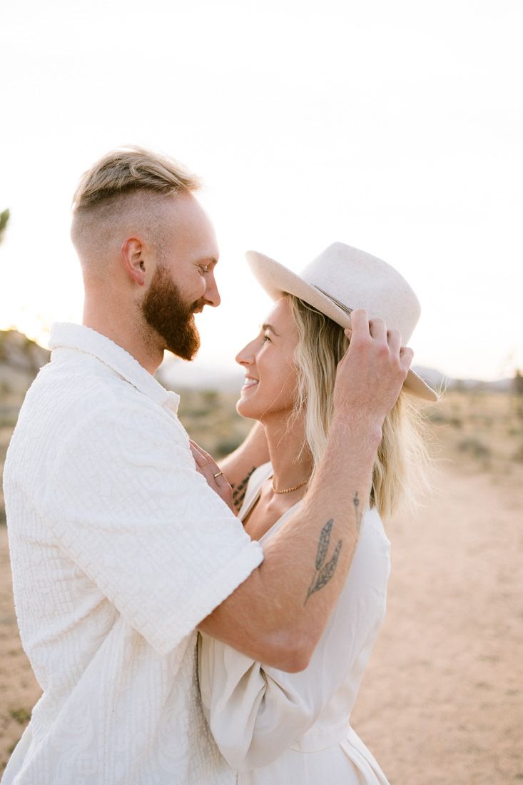 Intimate moment between couple in white outfits against desert backdrop.