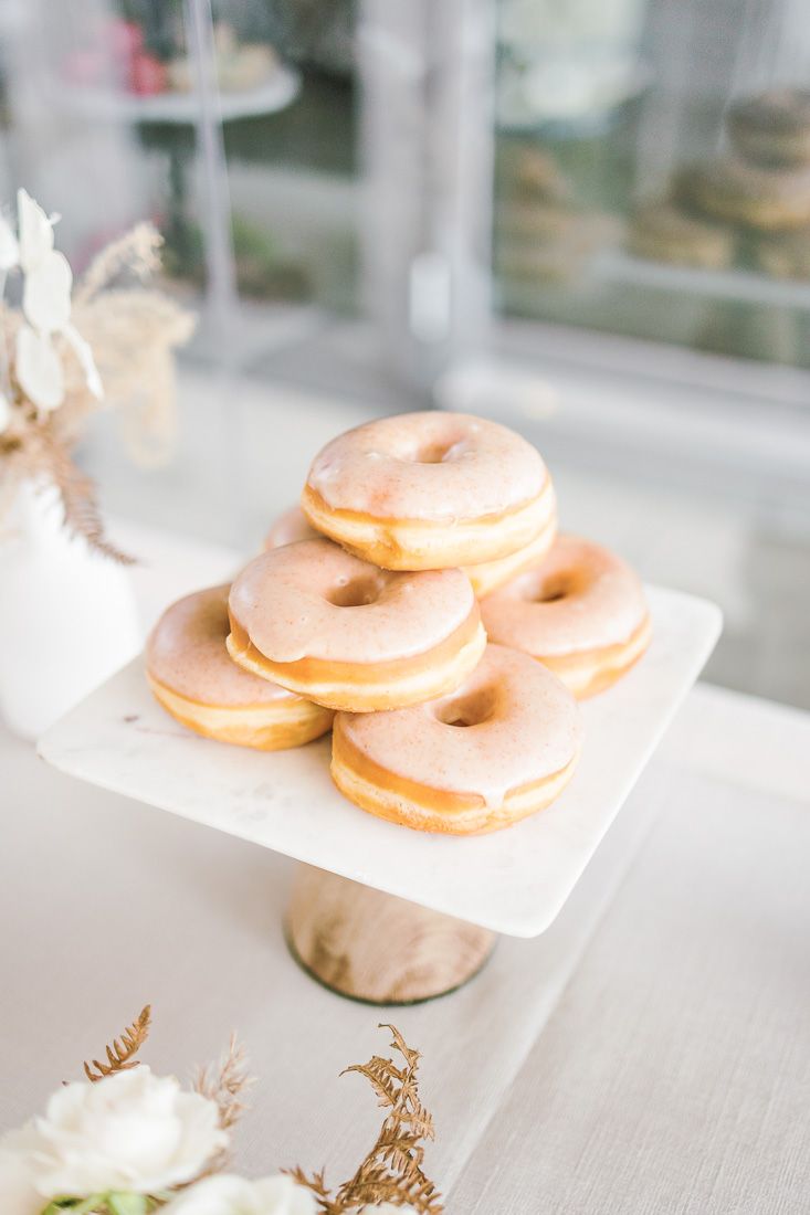 Stack of glazed donuts on a white pedestal cake stand in soft natural lighting.