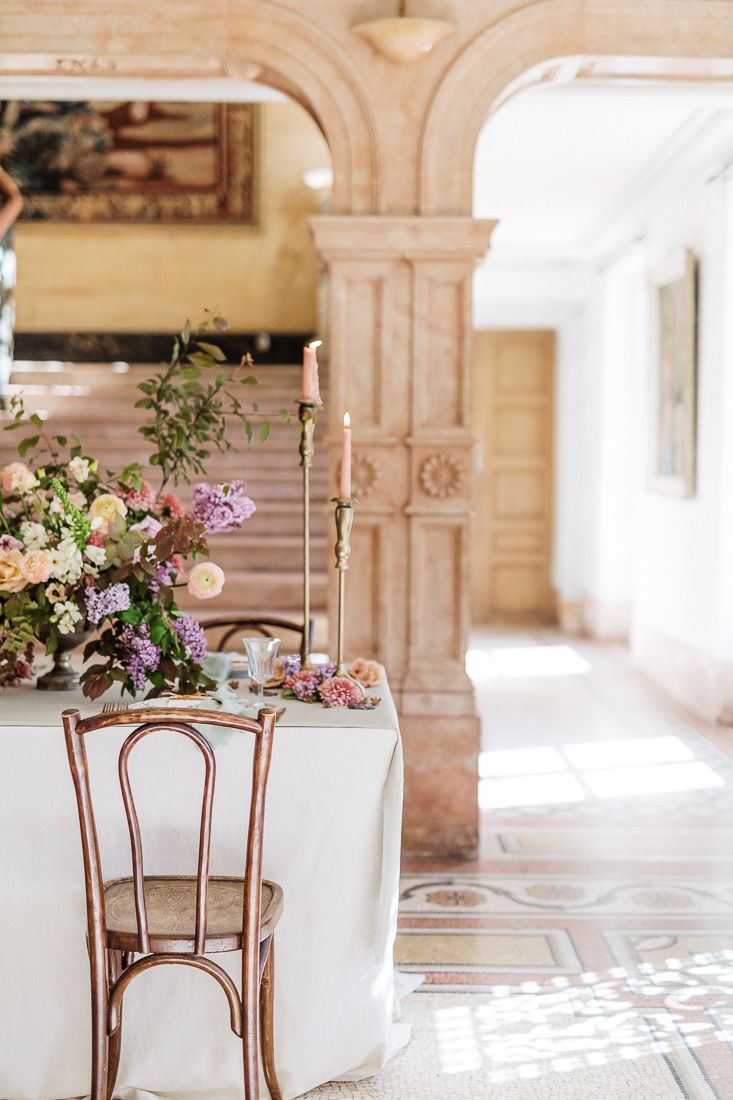 Romantic vintage table setting with bentwood chairs and lush floral centerpiece in an ornate room.