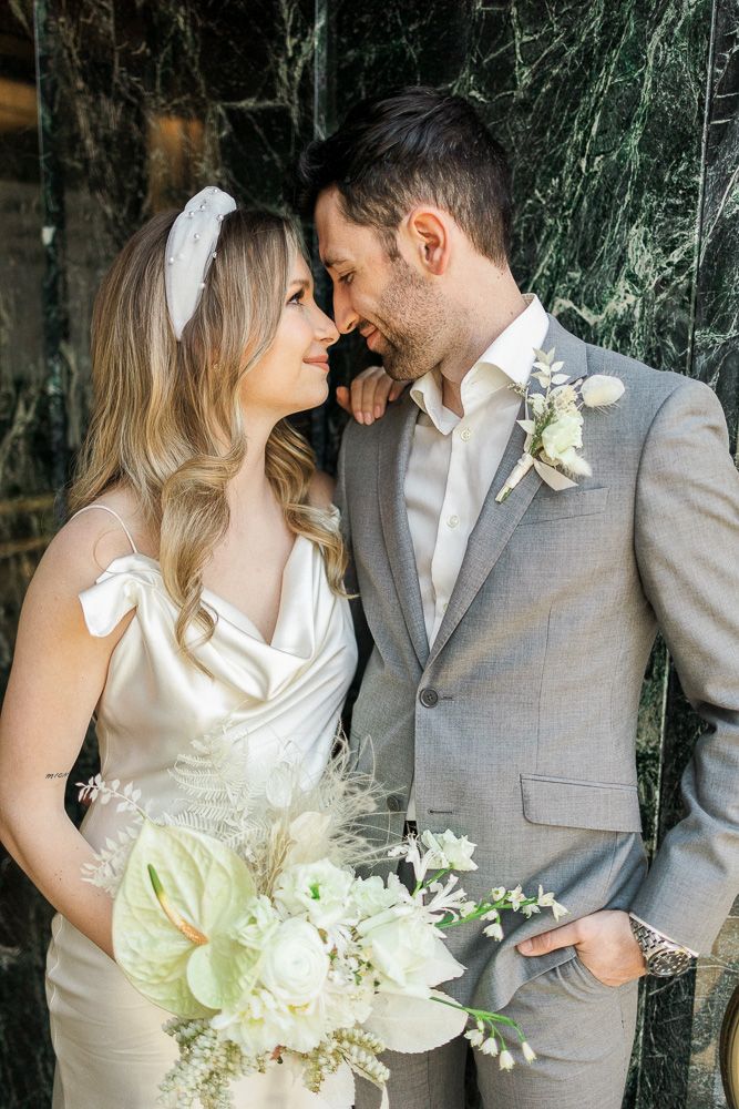 Romantic moment between couple with anthurium bouquet against marble backdrop.