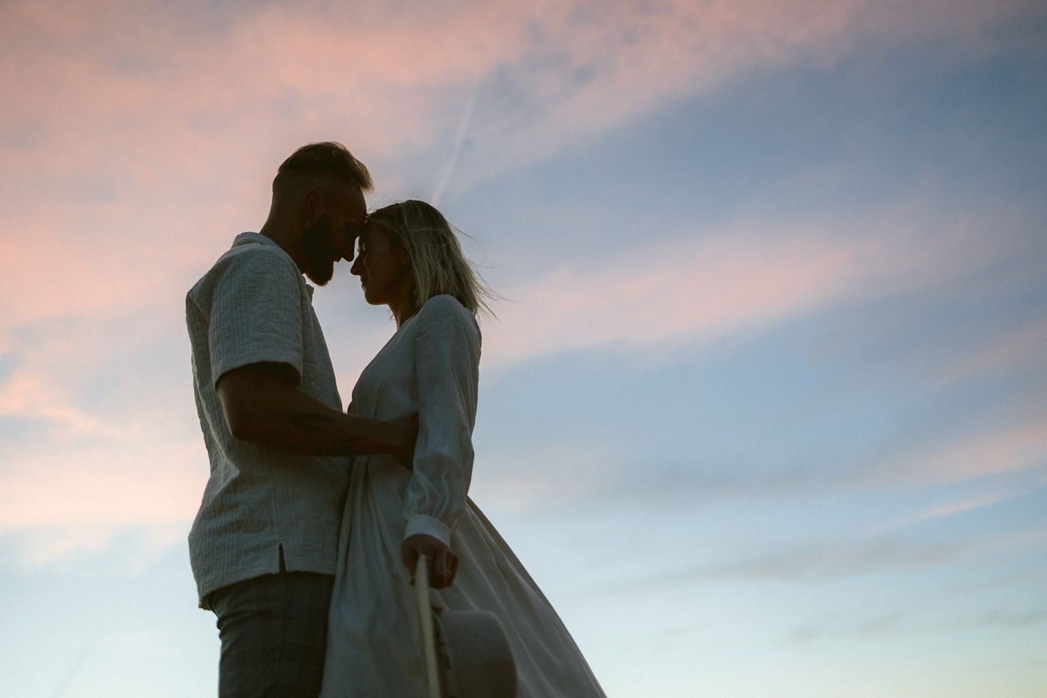 A romantic silhouette of a couple embracing against a pink and blue sunset sky.