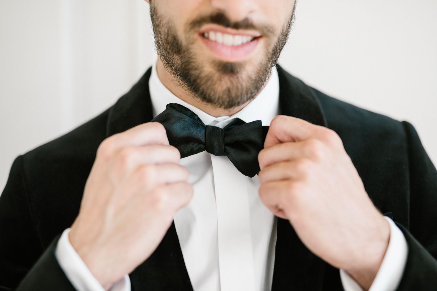 Close up of hands adjusting black bow tie on formal tuxedo.