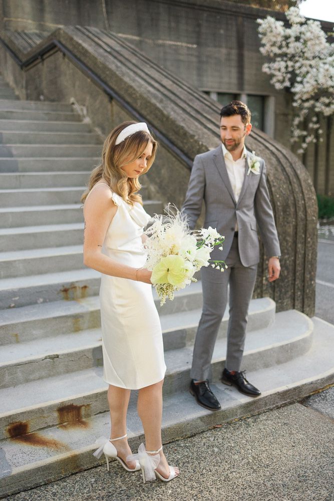 A bride in a white dress holding flowers while standing on concrete steps with her partner.