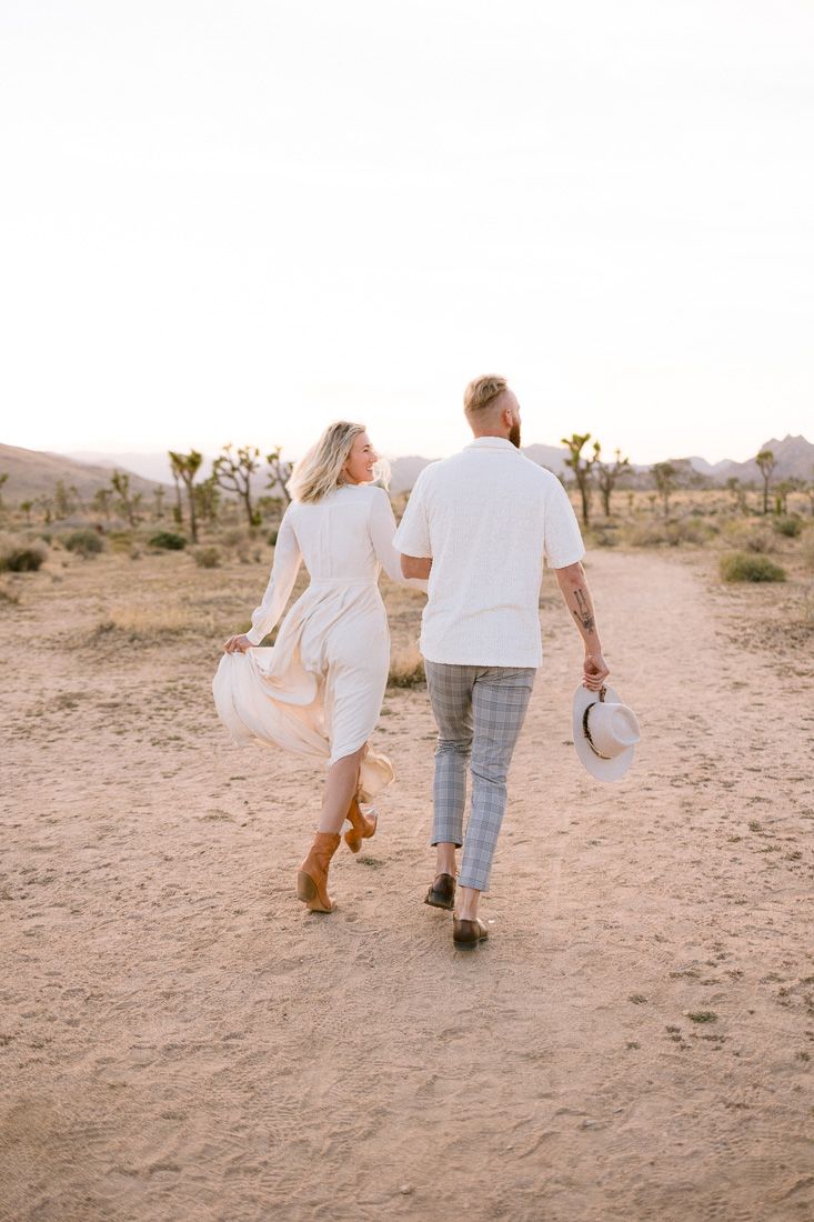 A couple walks together on a desert trail with Joshua trees in the background.