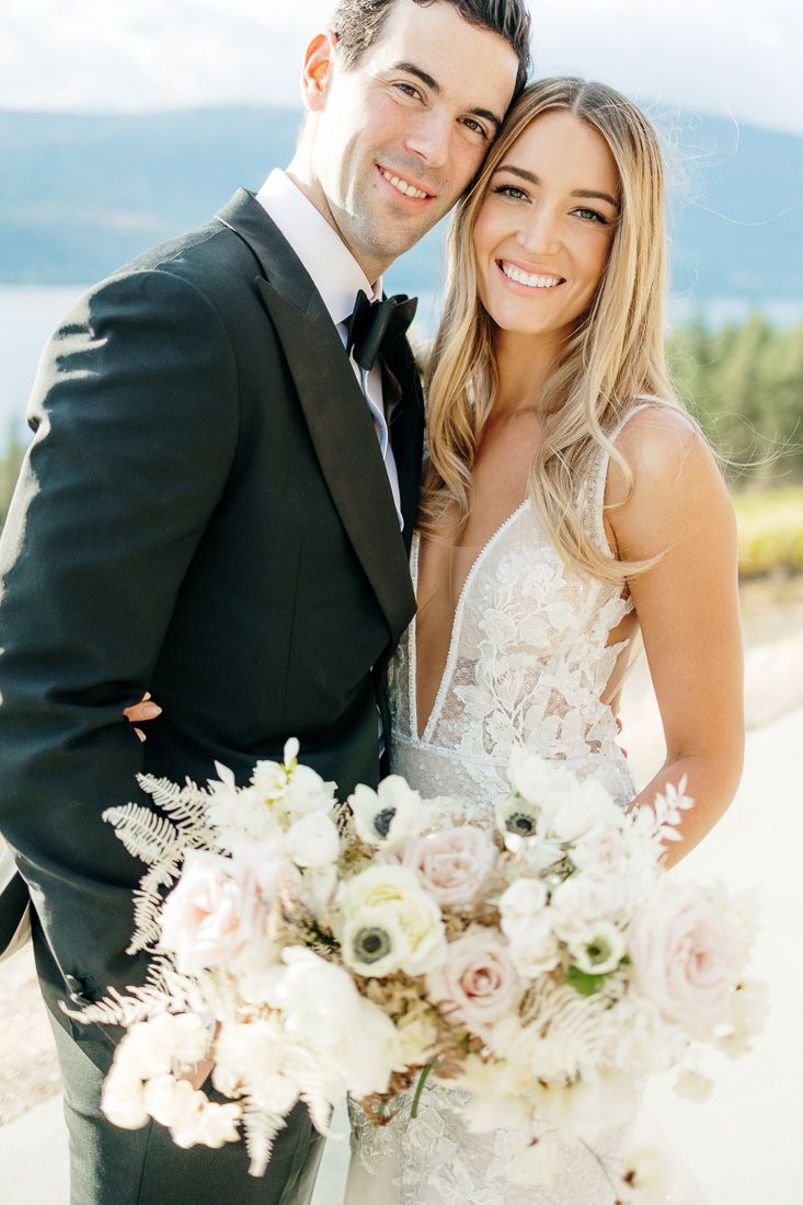 Sun-drenched wedding portrait with mountain backdrop and white floral bouquet.