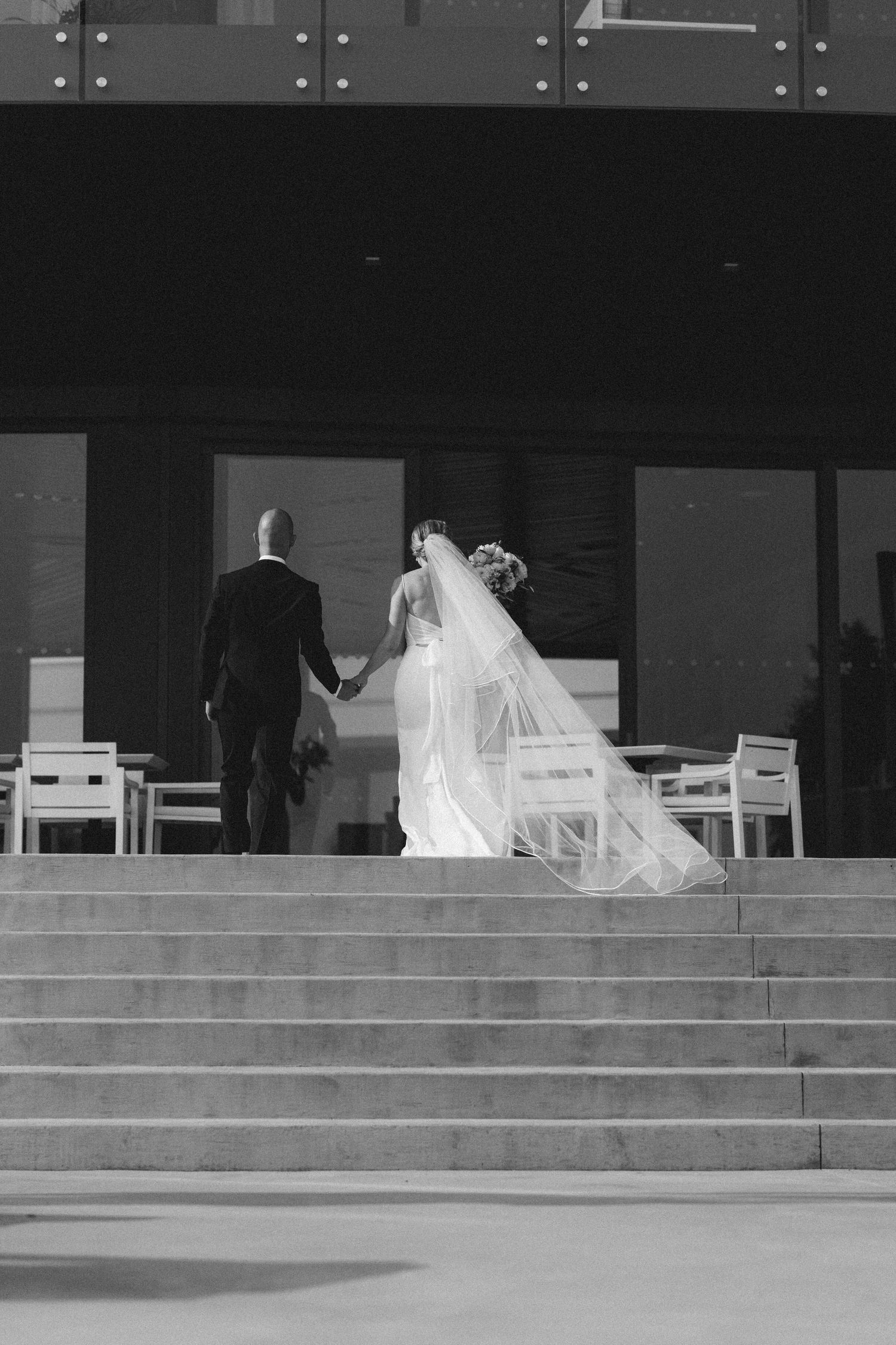 A black and white photo of a bride and groom on steps at their wedding venue.