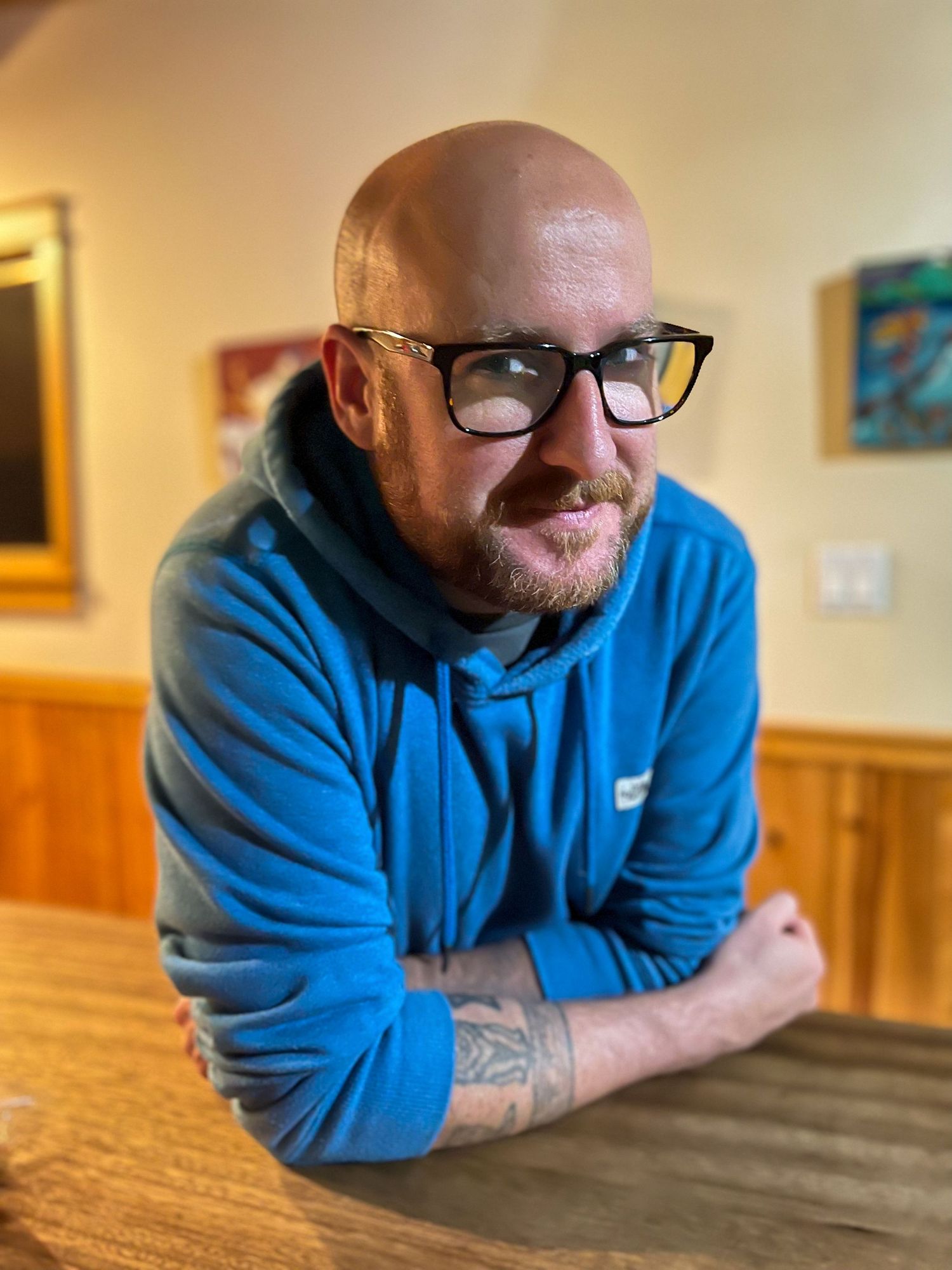 A person in casual blue attire leaning on wooden table indoors.