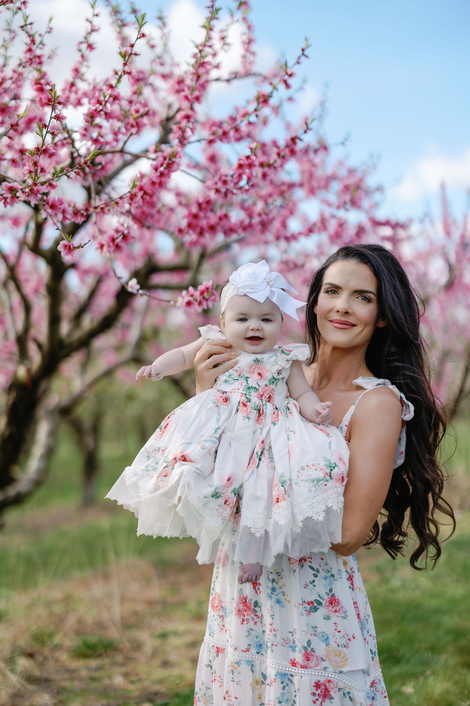 Beautiful portrait in a spring peach blossom orchard with matching floral dresses standing among pink blooming trees.