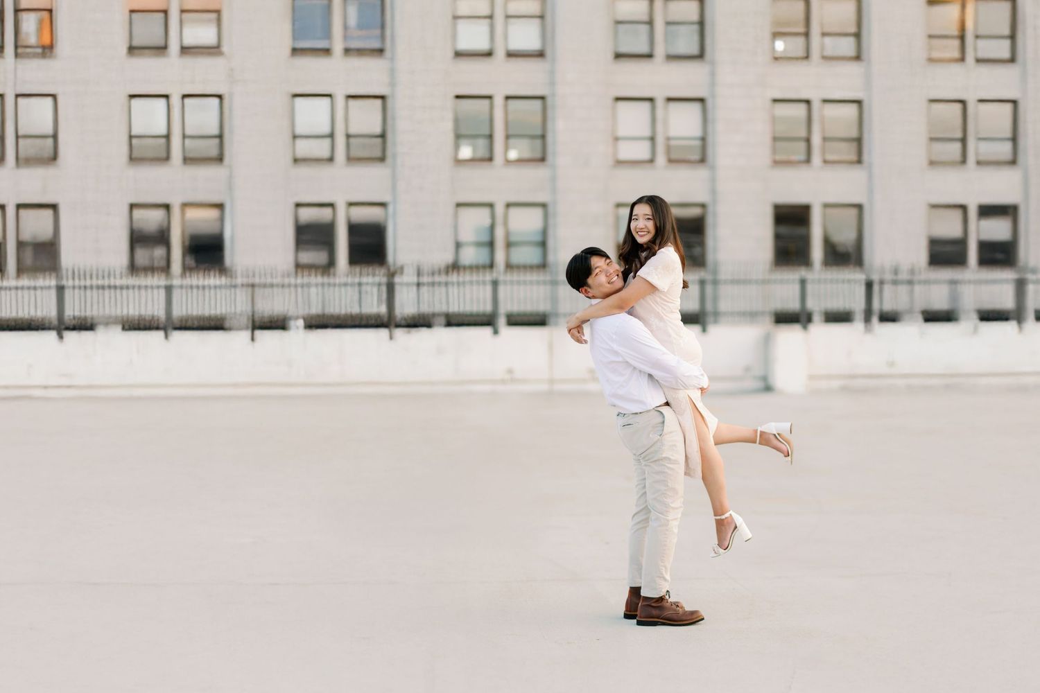 A joyful couple embraces on an urban rooftop with a backdrop of windows and architecture.