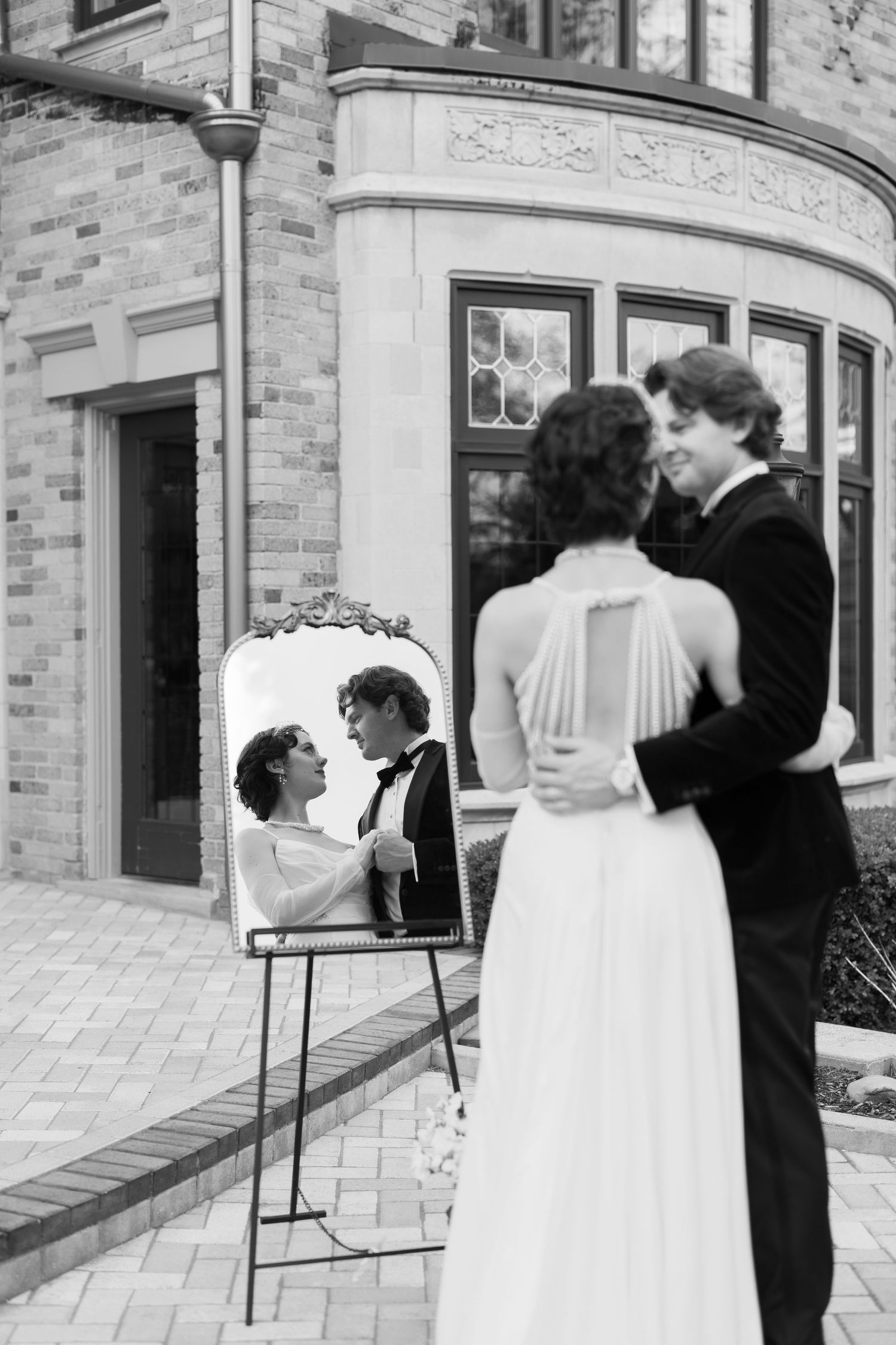 Black and white vintage photo showing a romantic couple in formal wear embracing, with their reflection in a mirror.