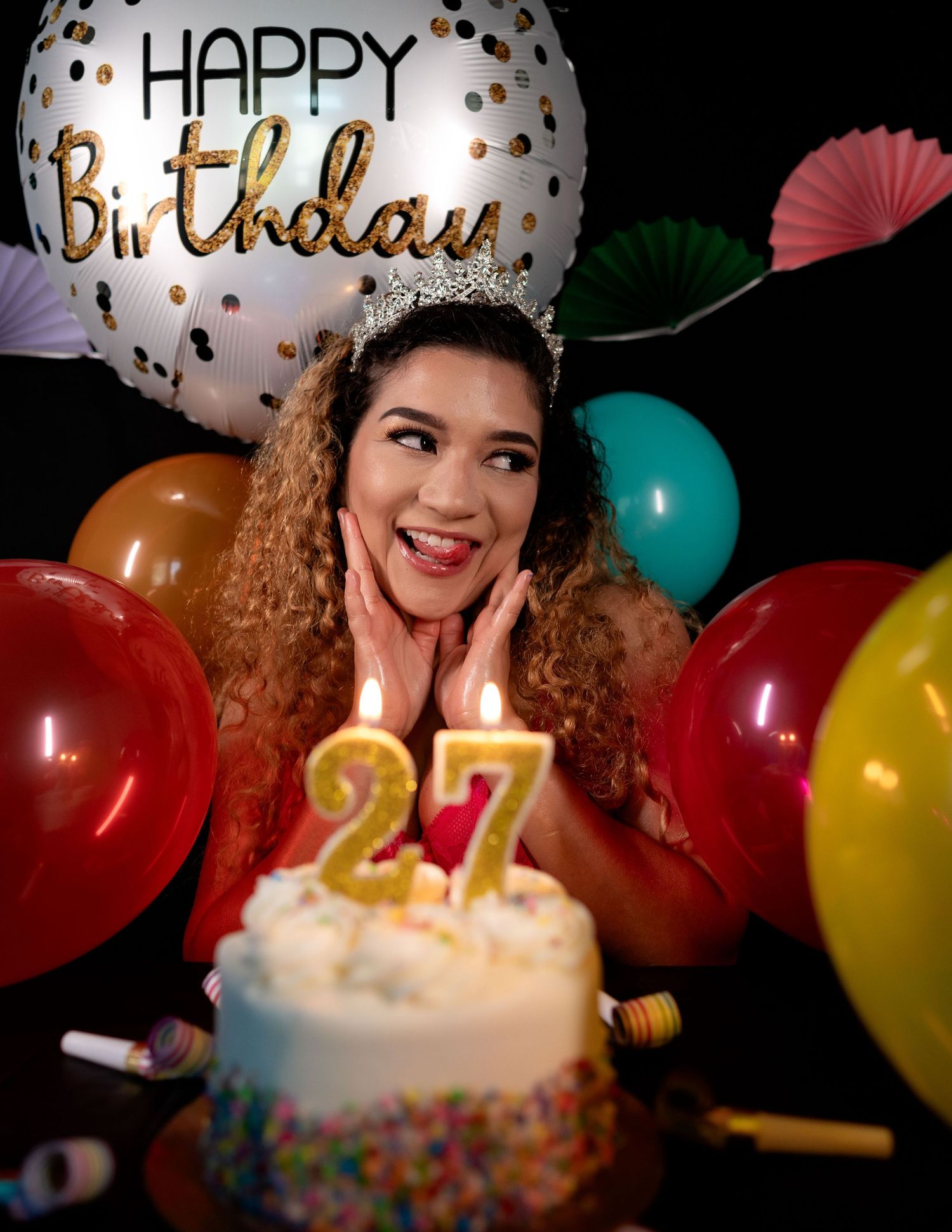Woman celebrating her 27th birthday with candles, balloons, and a Happy Birthday balloon behind her.