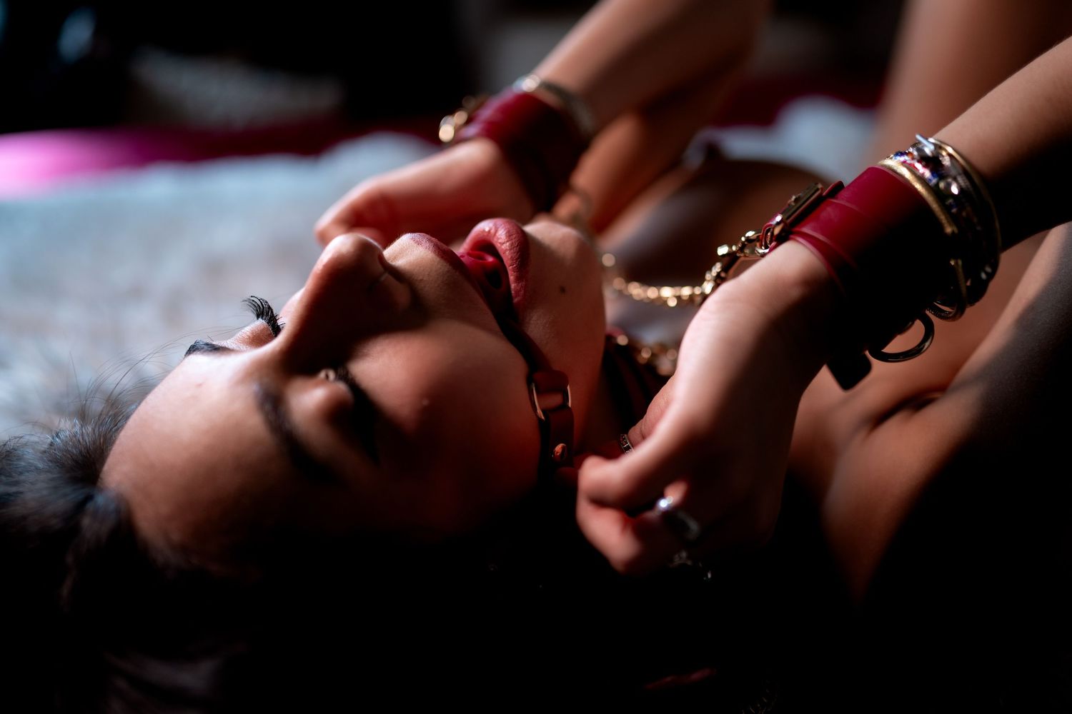 Close-up of a woman lying down adorned with red and gold bangles and jewelry in dramatic lighting.