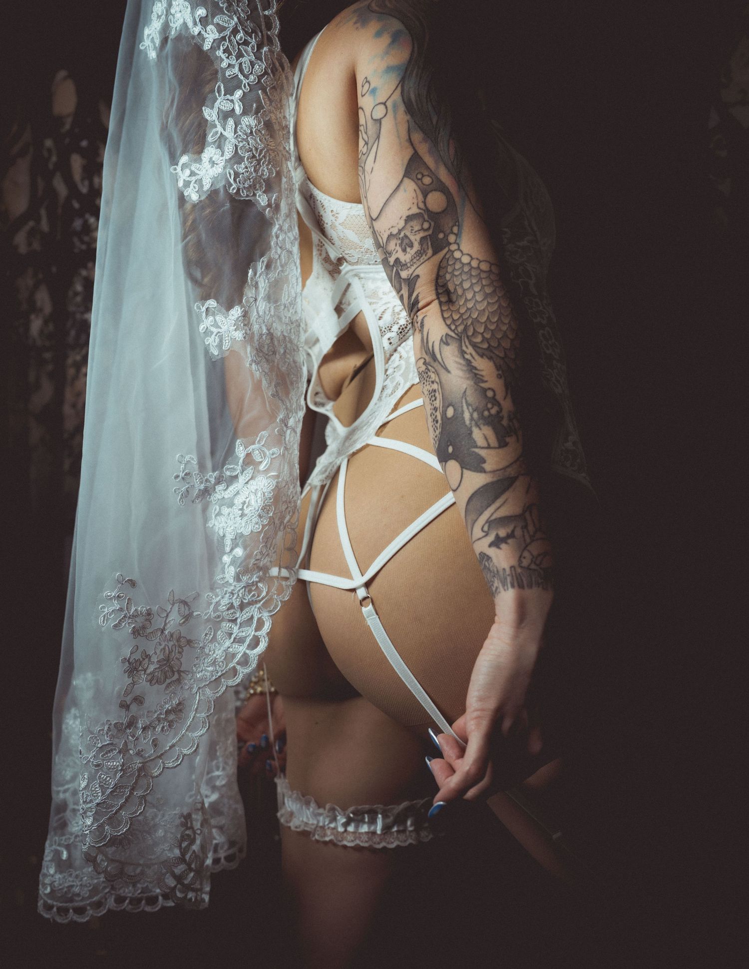 Tattooed bride in white lingerie and garter set with lace veil, boudoir wedding photography.