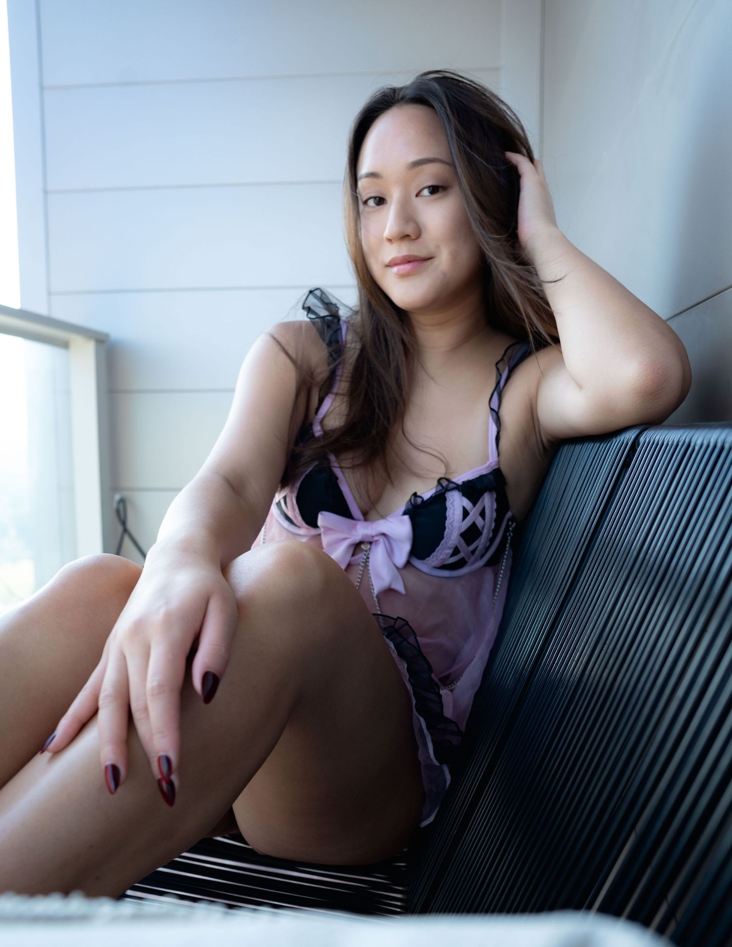 A person in a purple top lounges casually on a striped couch while taking selfie photos.
