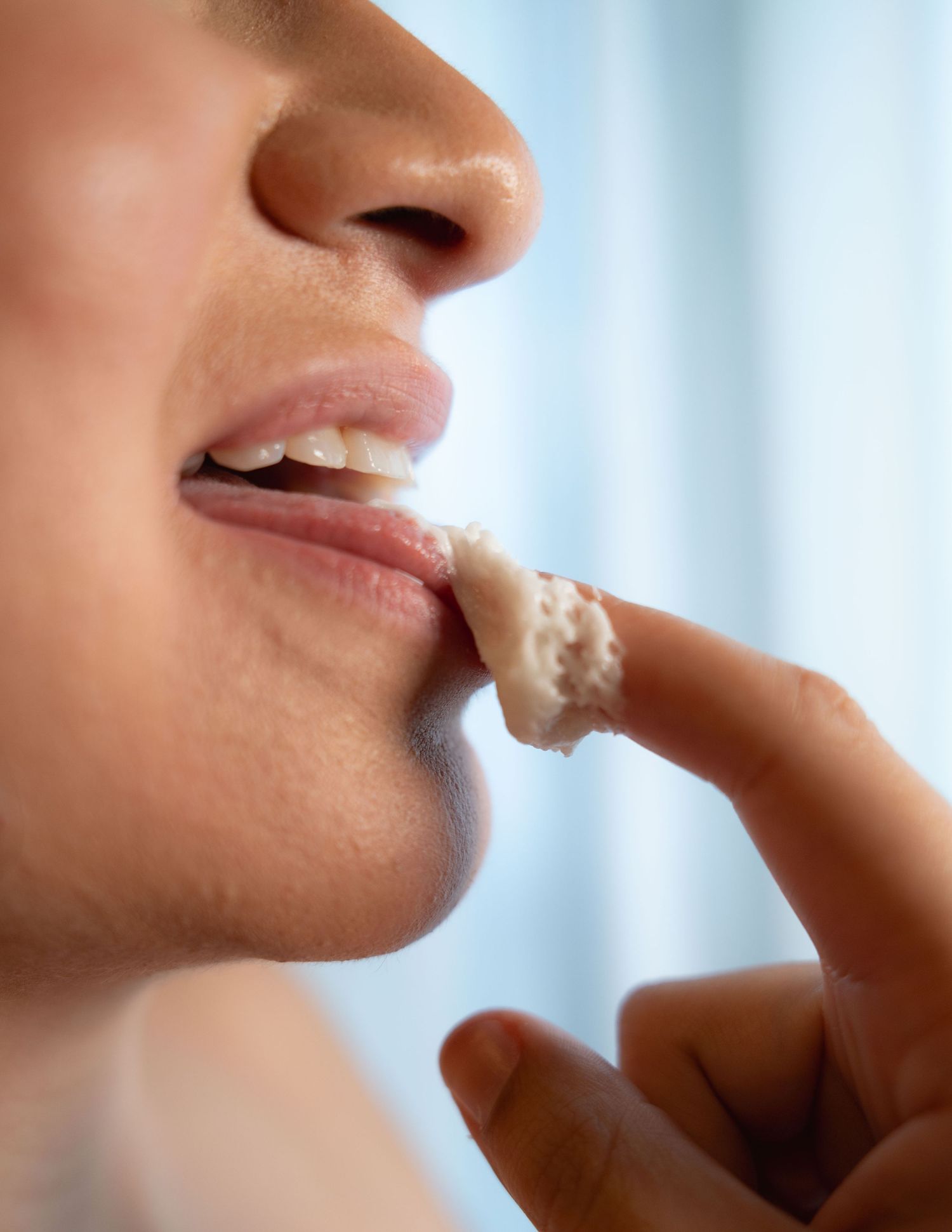 Close-up of a person applying white cream to their lips with their finger for moisturizing lip care treatment.