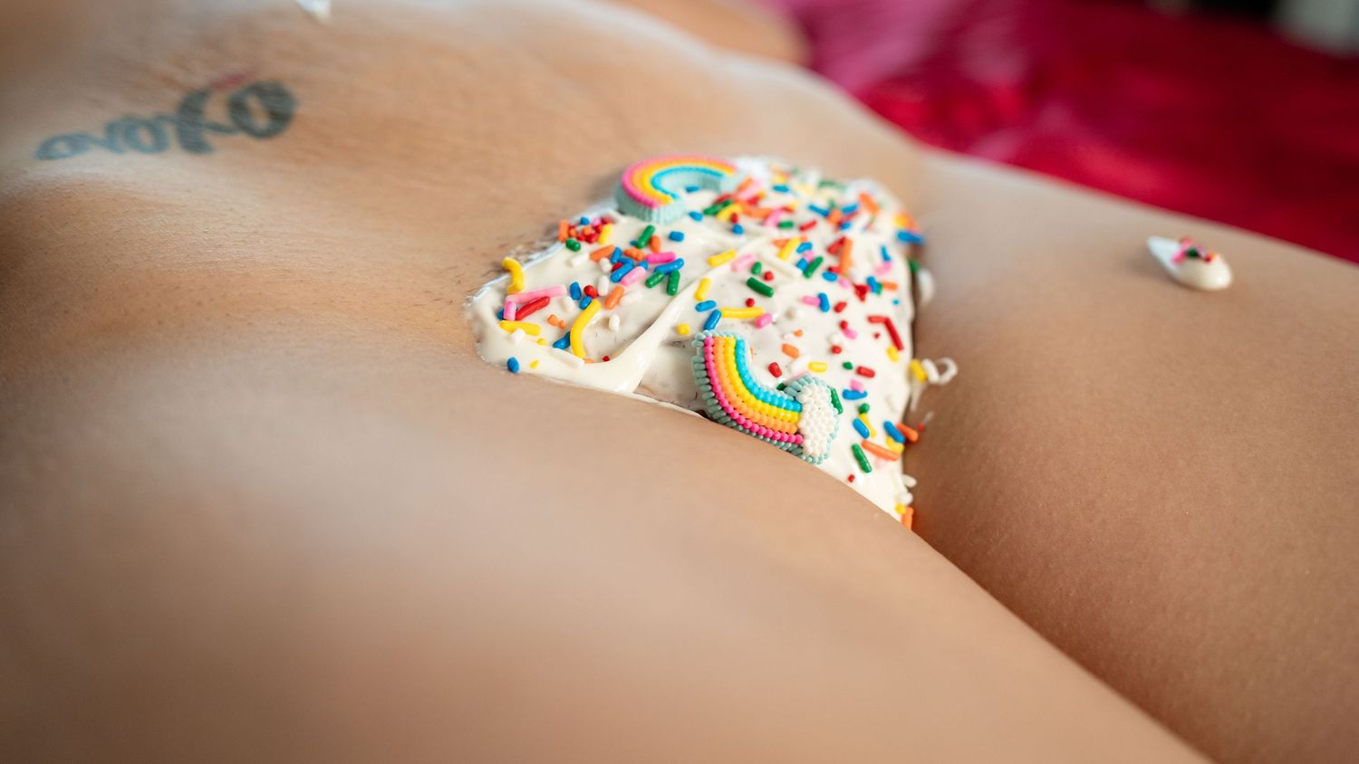 Rainbow sprinkle decorated white chocolate candy piece with colorful confetti toppings resting on skin.
