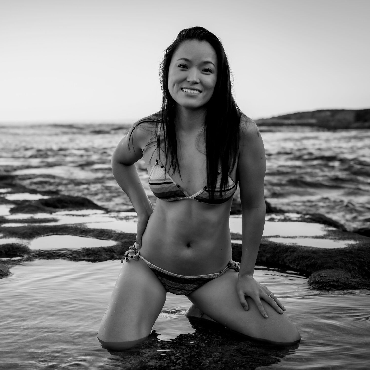 Black and white photo series of someone posing in a swimsuit on rocky beach with ocean waves in background.