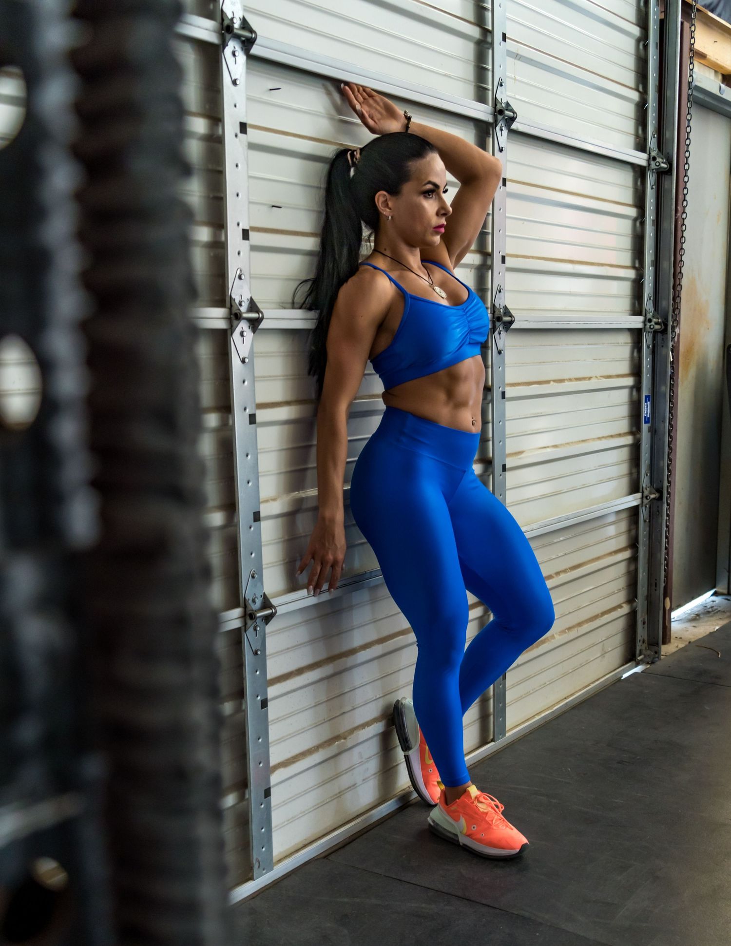 Athlete in bright blue workout attire performs wall sit exercises against white storage door.
