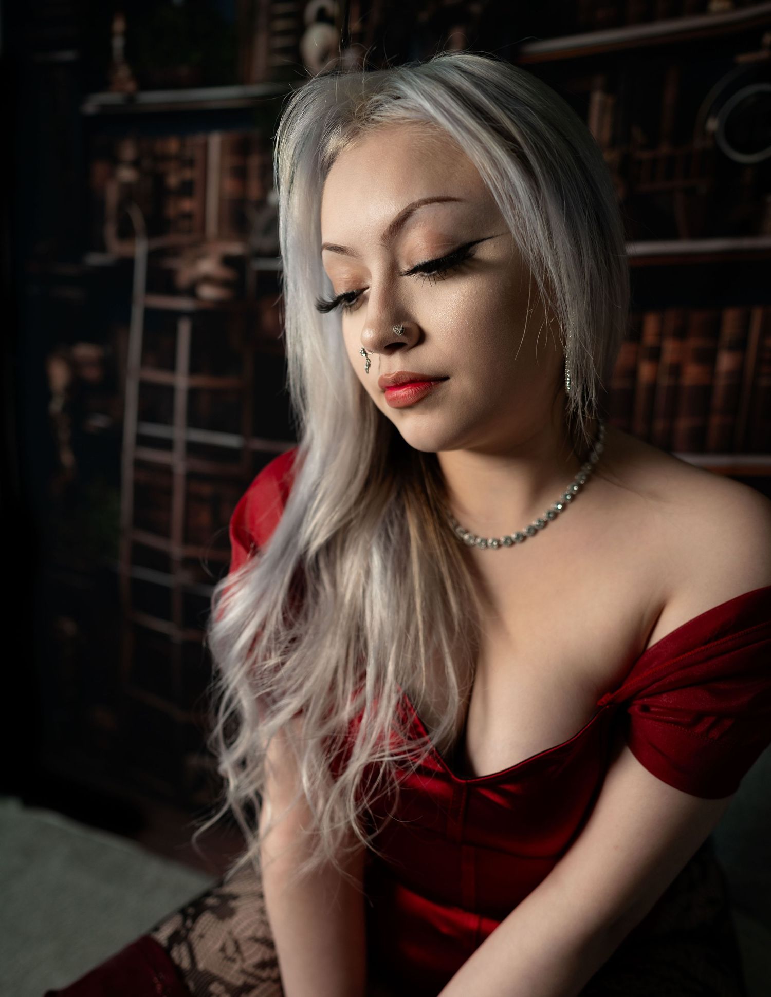 A figure in a red dress poses against a dark background with dramatic lighting and silver hair.