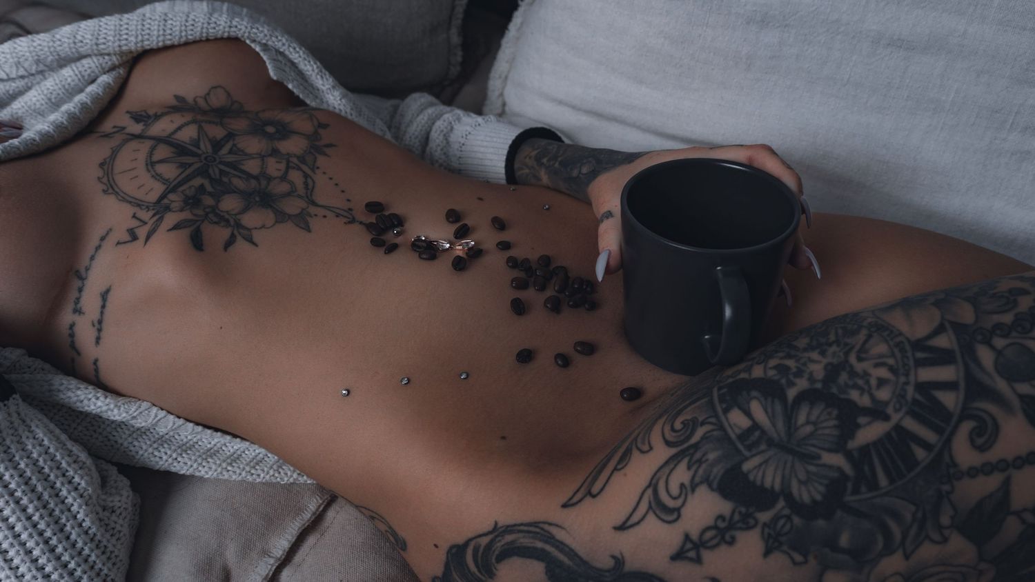 Artistic photo of tattooed torso with coffee cup resting on bare skin.