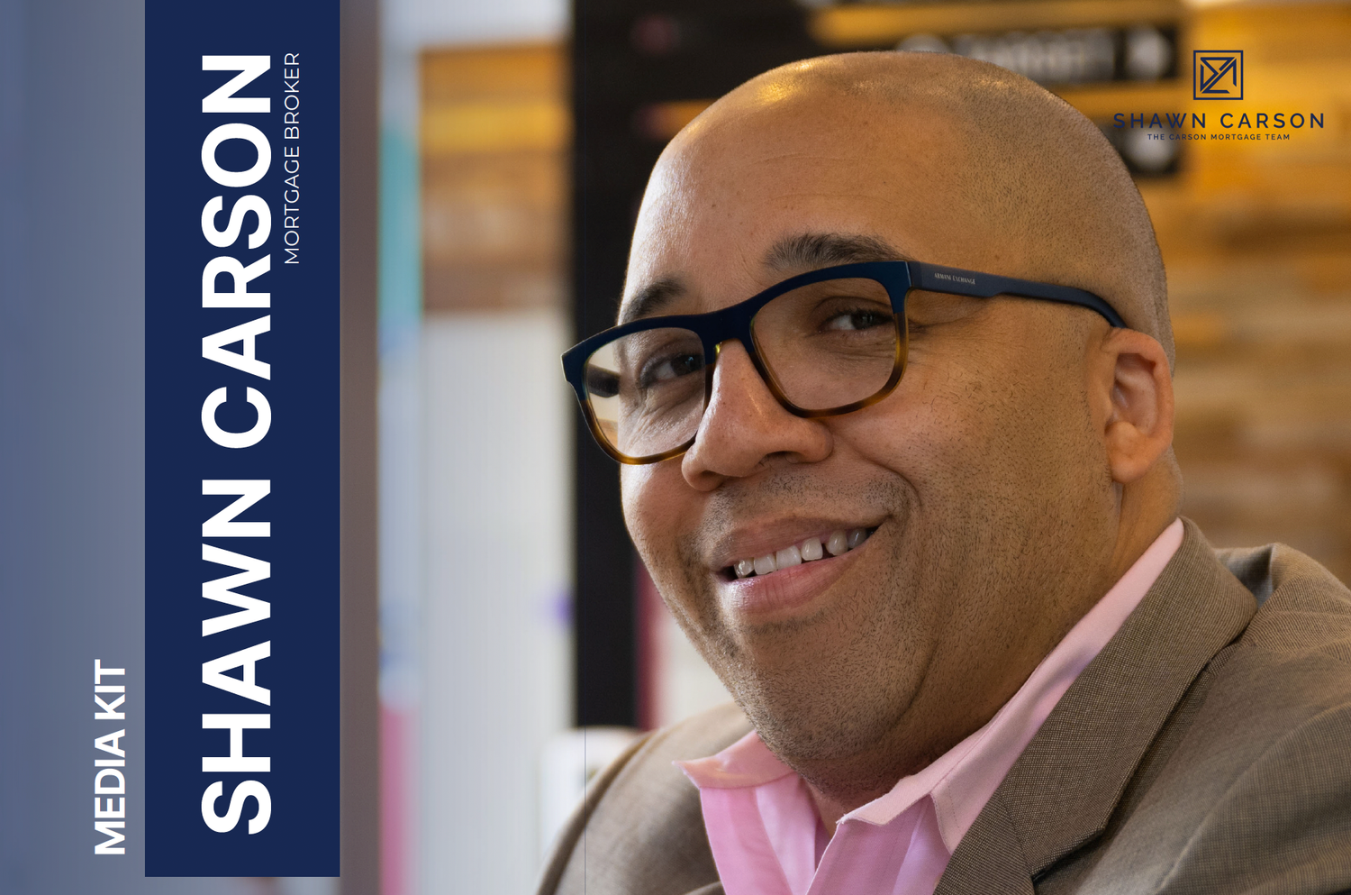 Professional wearing glasses and a pink dress shirt smiles while seated in a brown suit jacket.