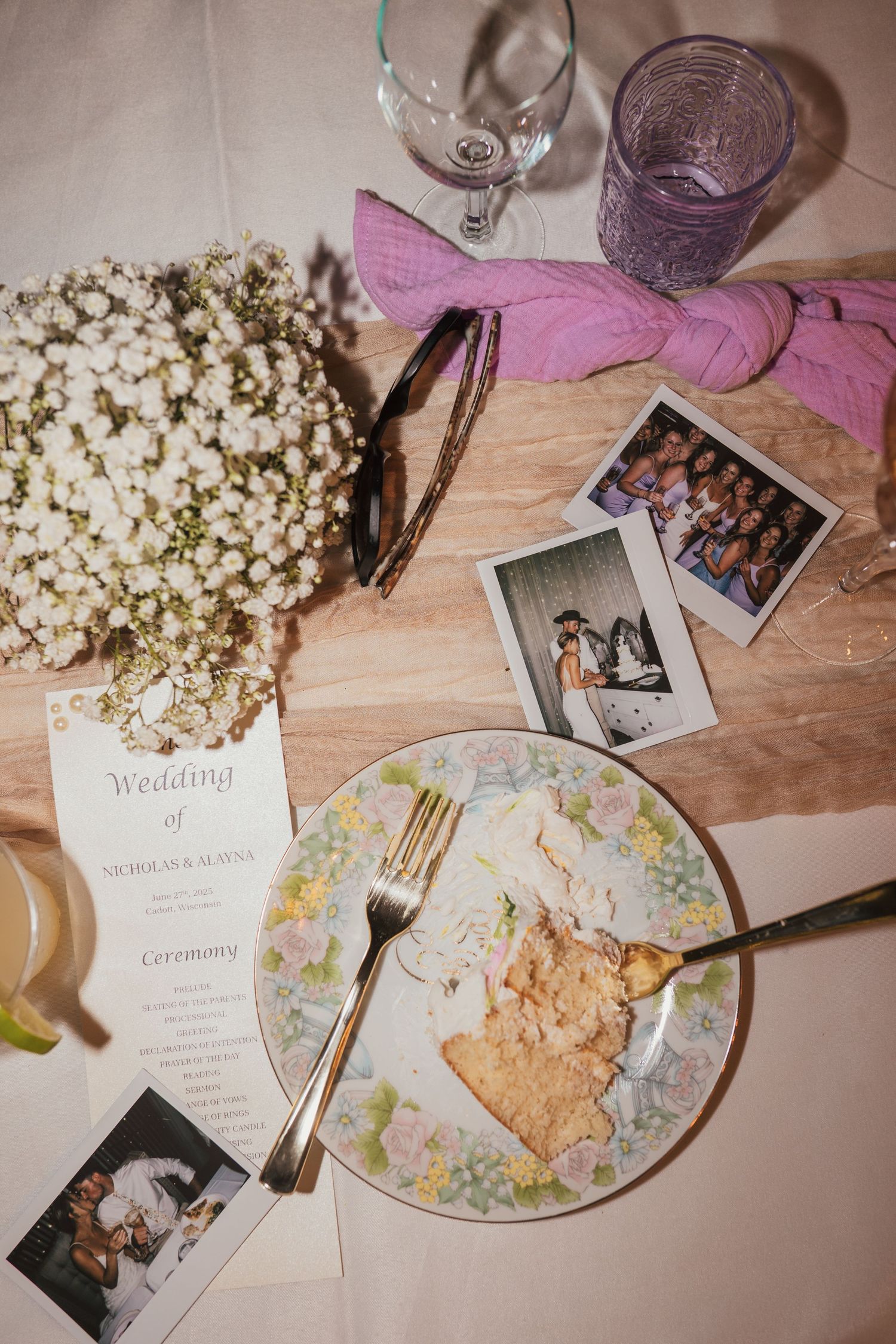 Wedding reception details with wine glasses, invitation cards, floral arrangements and snacks on a wooden table.
