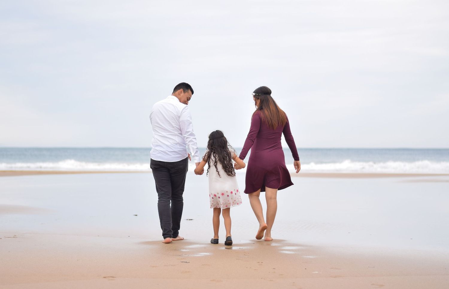 Authentische Familienfotografie: Mutter, Vater und Tochter beim Spaziergang am Strand, ungestellte Lifestyle-Momente.
