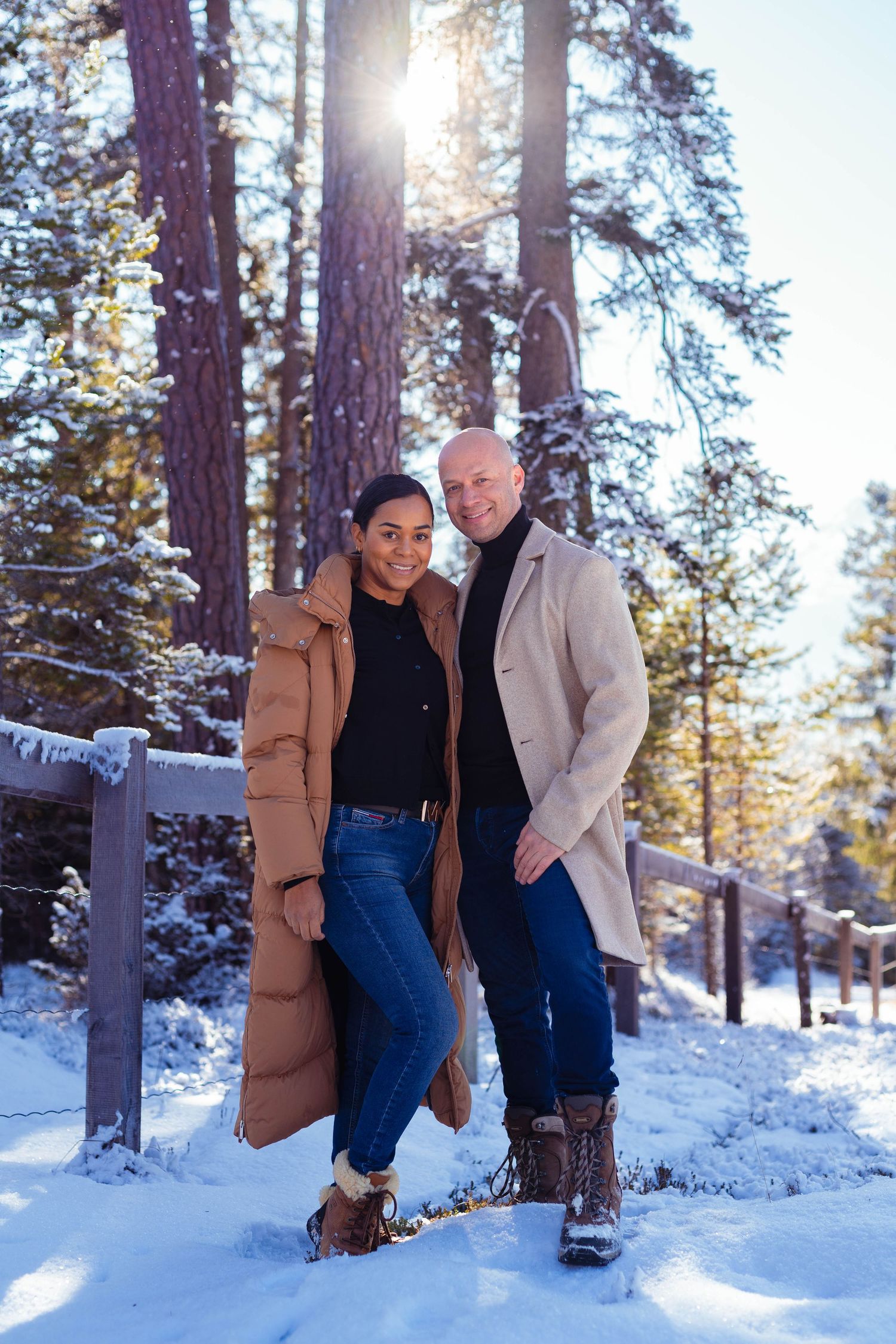 Elegantes Editorial-Paarportrait am Holzzaun in der verschneiten Winterlandschaft von Davos.
