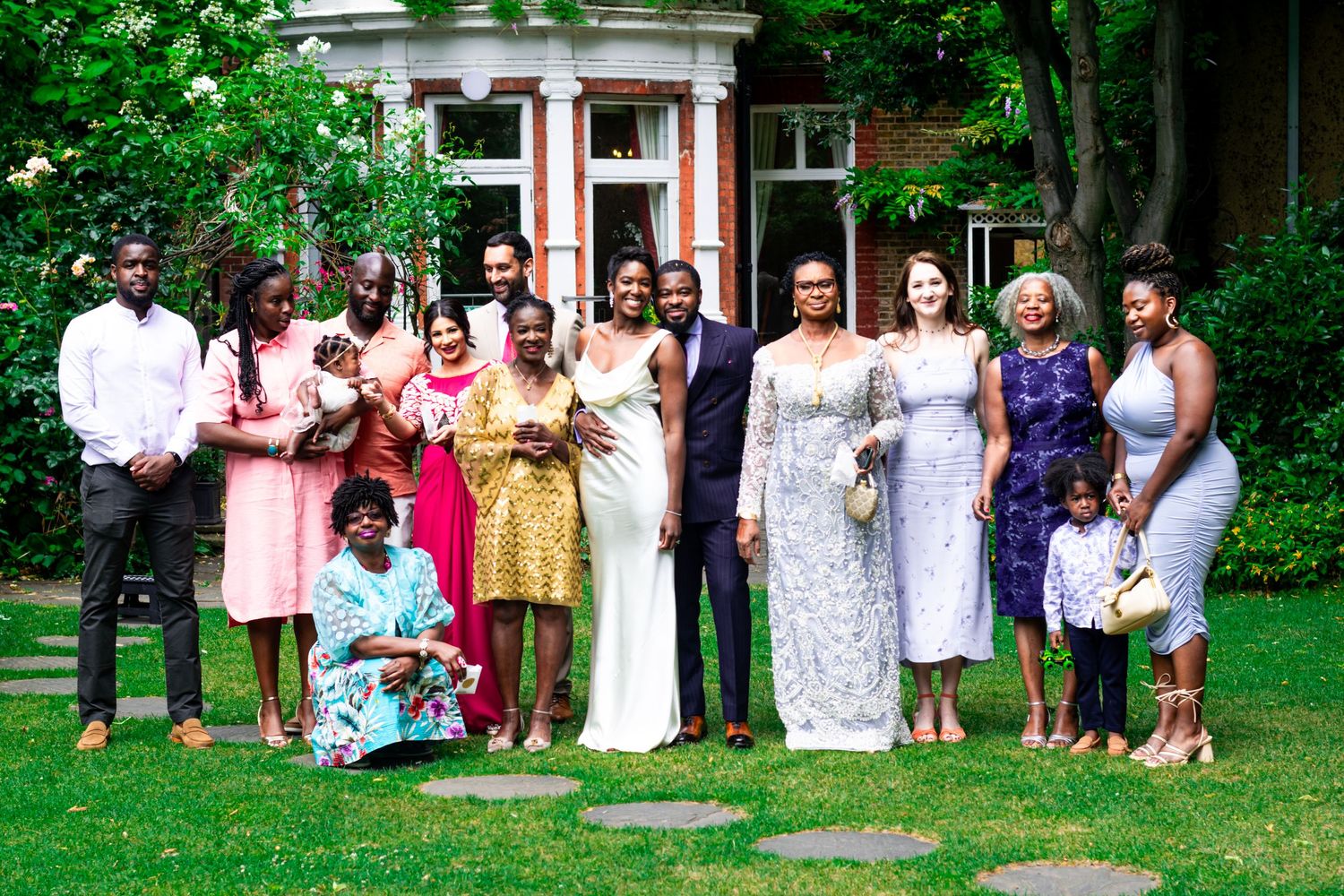 Bride and groom standing together outdoors, surrounded by wedding guests in formal attire.