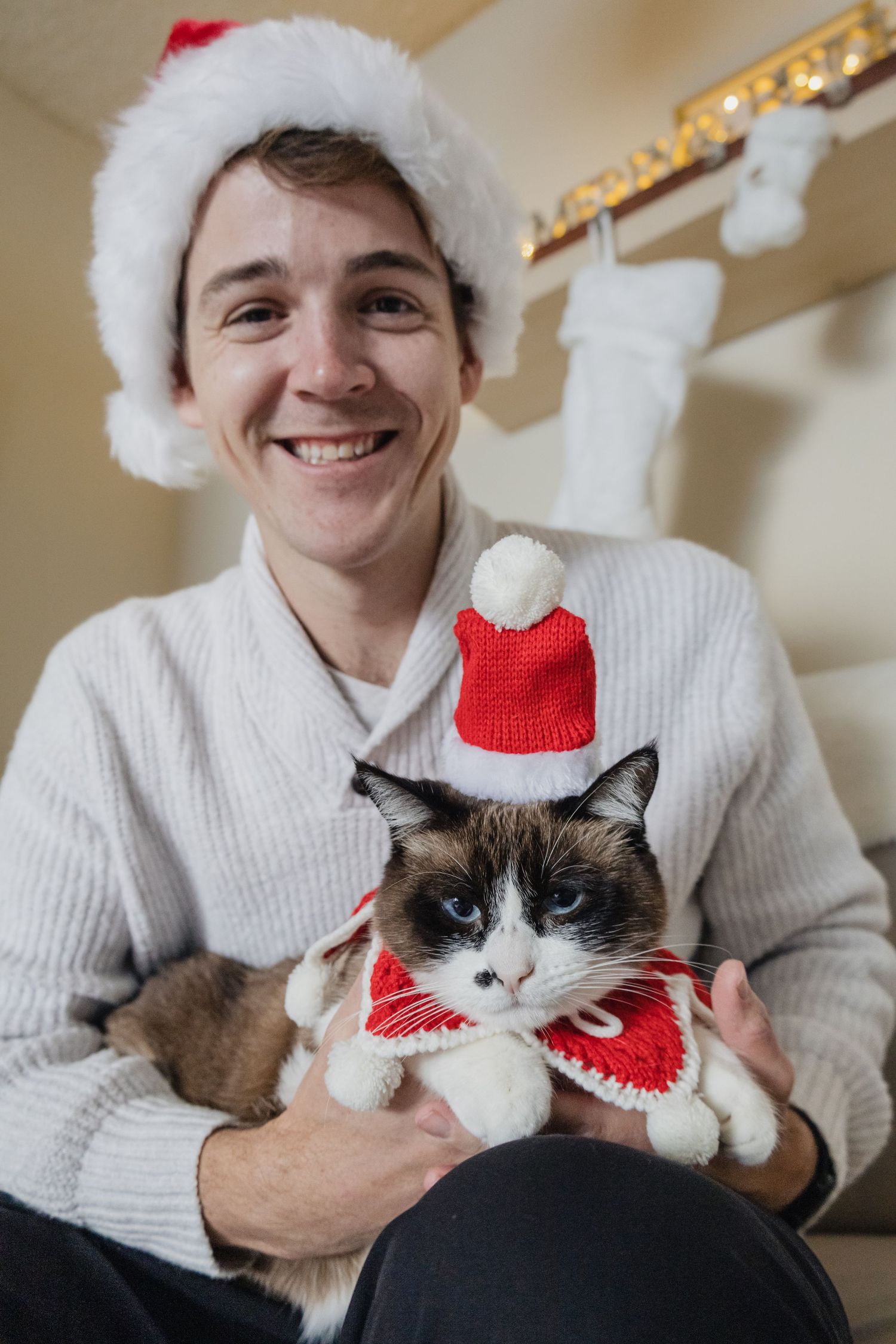 A picture by Sara Pang (MSK Productions) of a man holding a cat in a Christmas hat and collar.