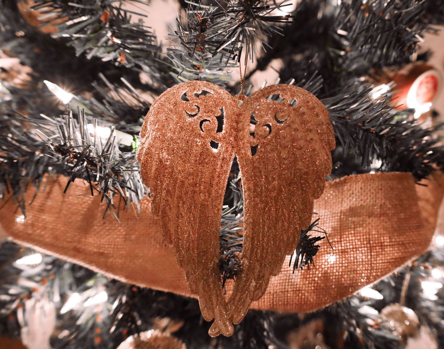 A picture by Sara Pang (MSK Productions) of a Christmas ornament of golden wings on a lit Christmas tree.