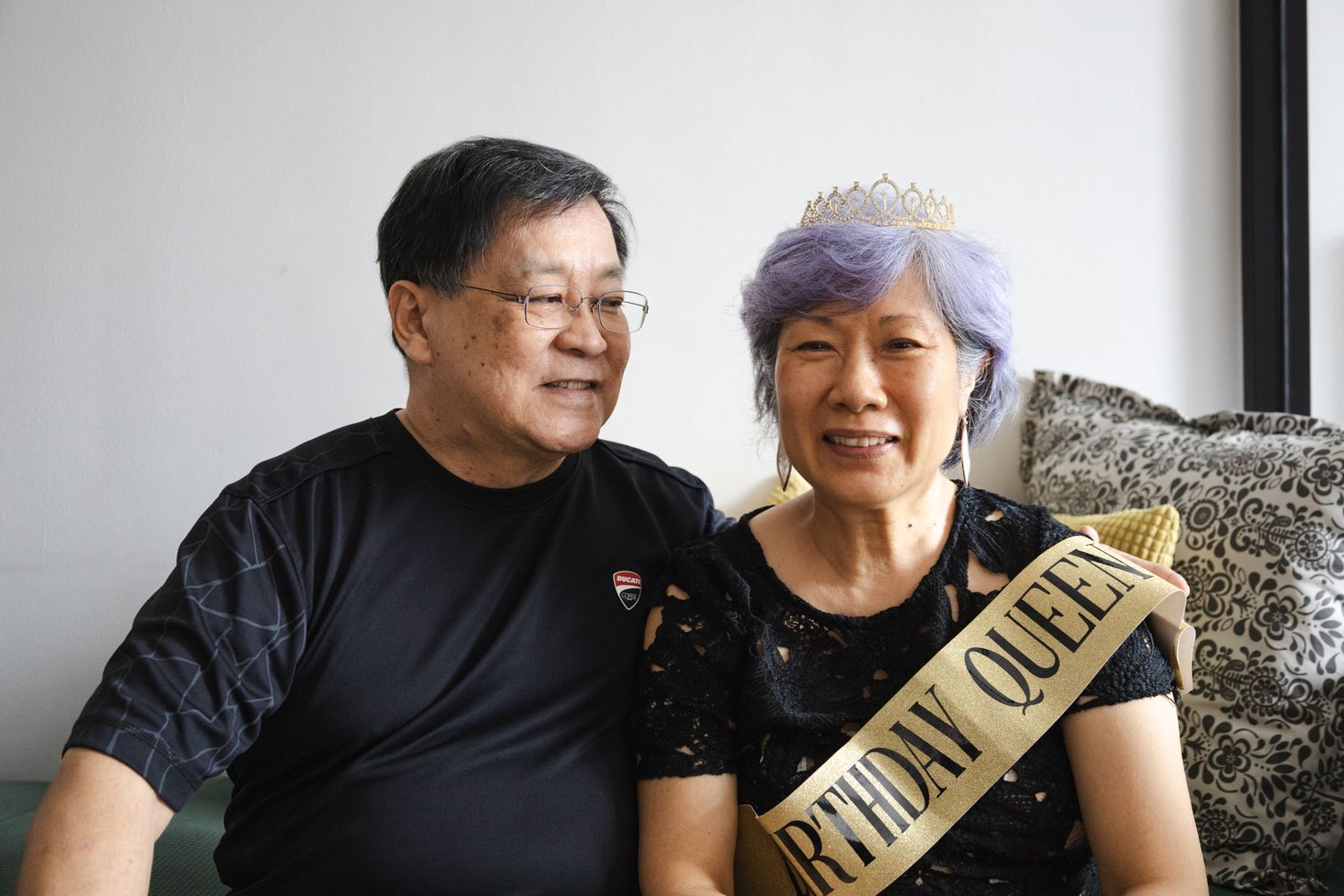 A picture by Sara Pang (MSK Productions) of an elderly man lookin at his wife as she wears a golden crown and golden birthday queen sash.